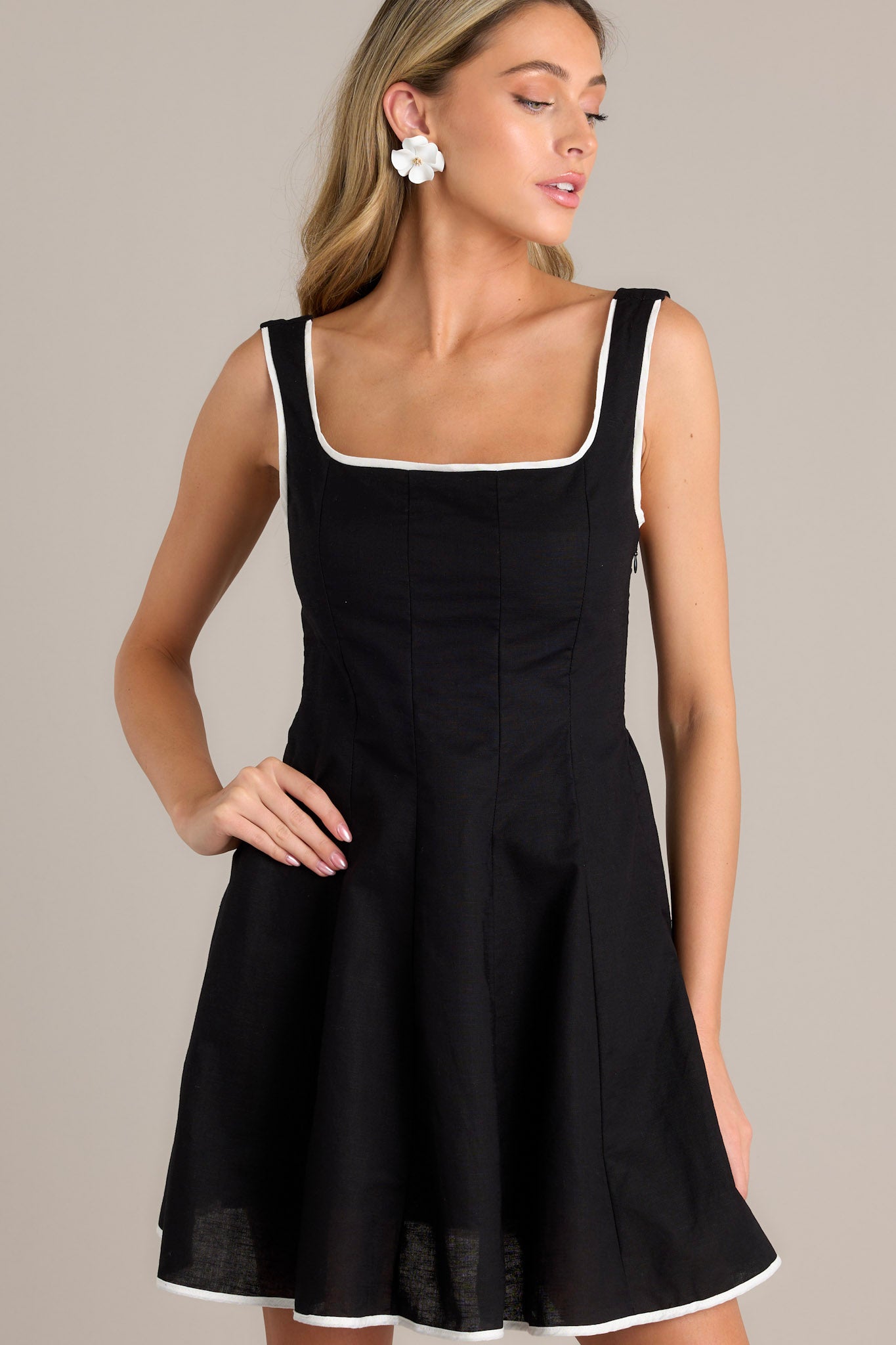 Front view of a black mini dress showcasing a square neckline, discrete side zipper, and white trim along the hem and neckline.