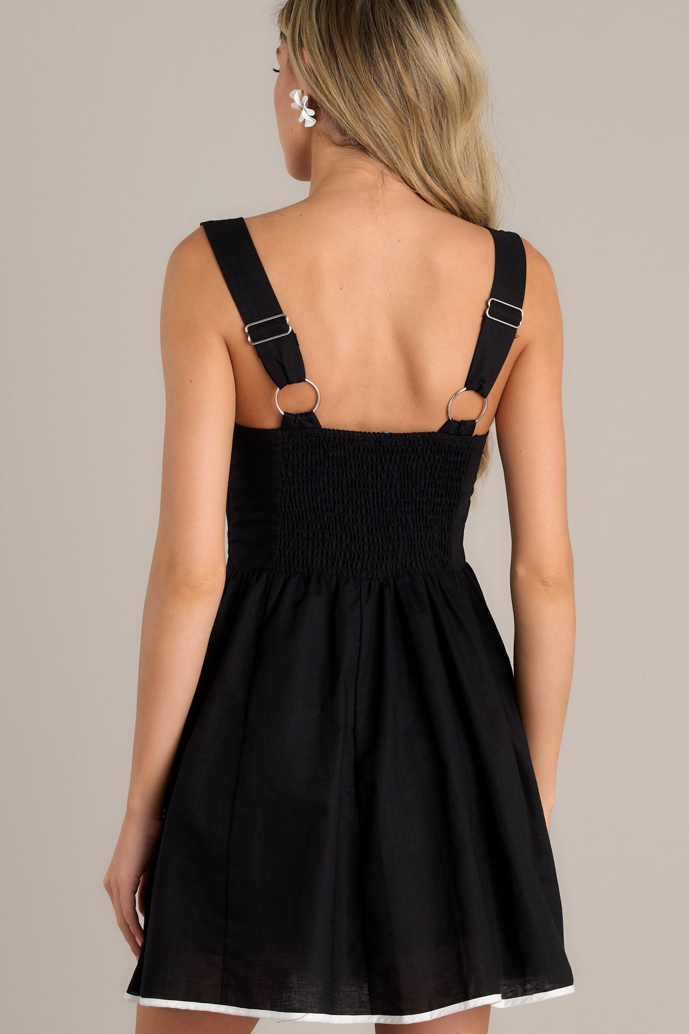 Back view of a black mini dress featuring thick adjustable straps, a smocked back insert, and contrasting white trim.