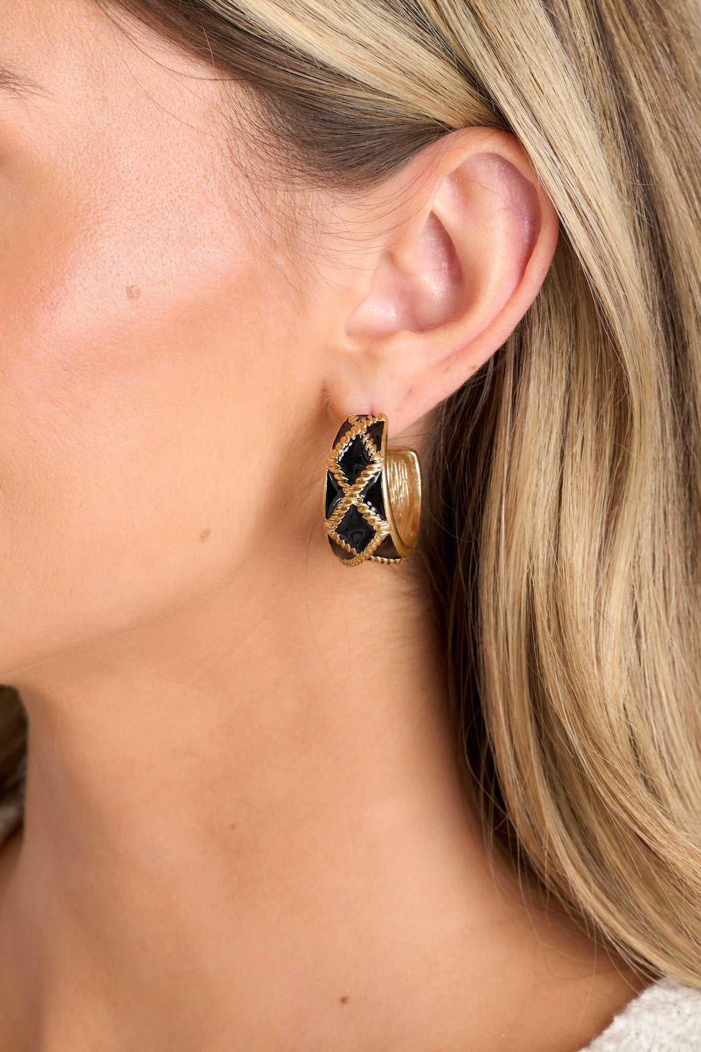 Close-up view of these black earrings that feature an incomplete hoop design, a gold textured design, and secure post backings.