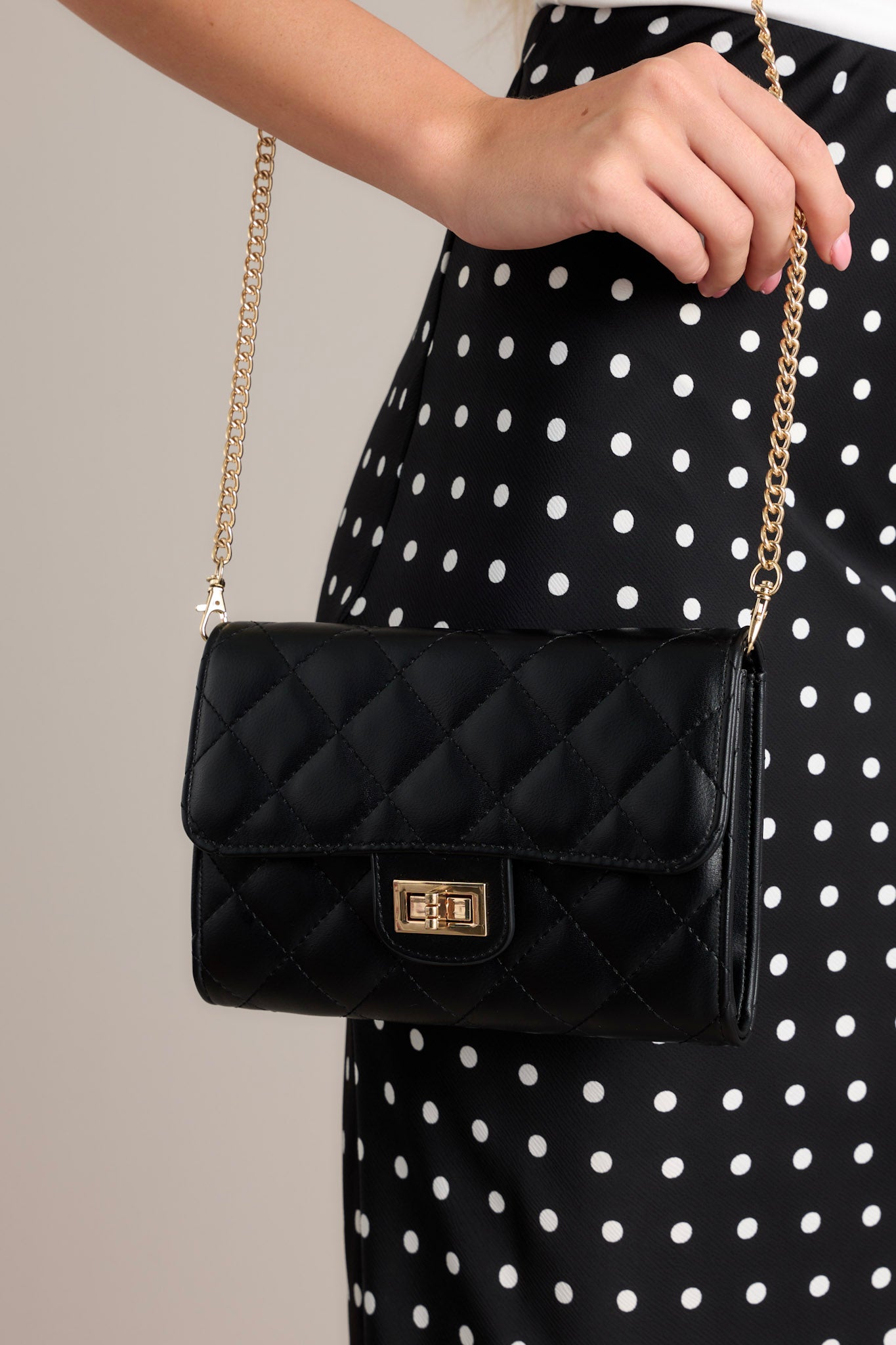 Front view of this black bag that features gold hardware, a quilted design, turn lock closure, a zipper pocket inside, and a detachable chain shoulder strap.