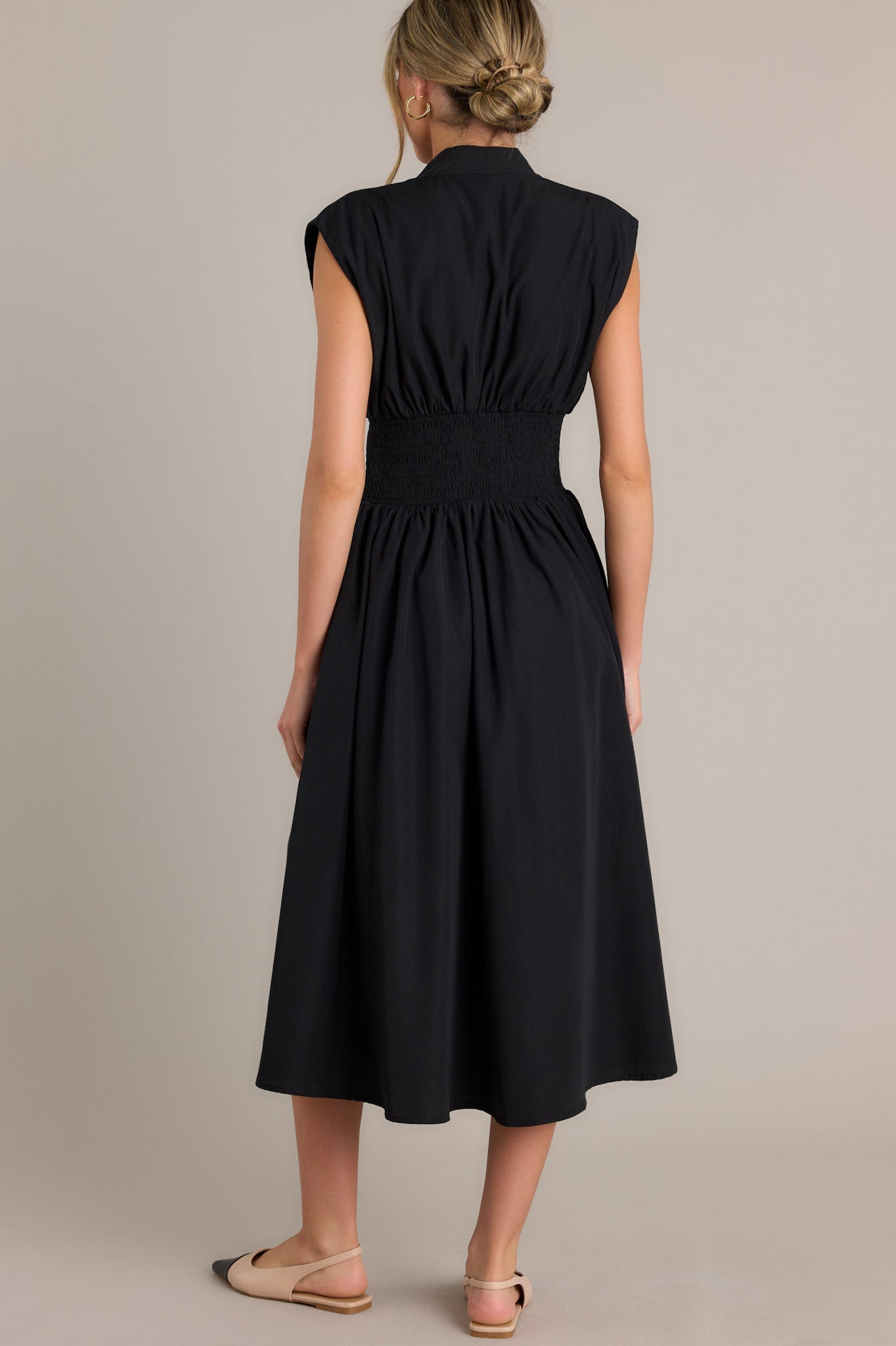 Back view of a black midi dress highlighting the padded shoulders, smocked waist, and overall fit.