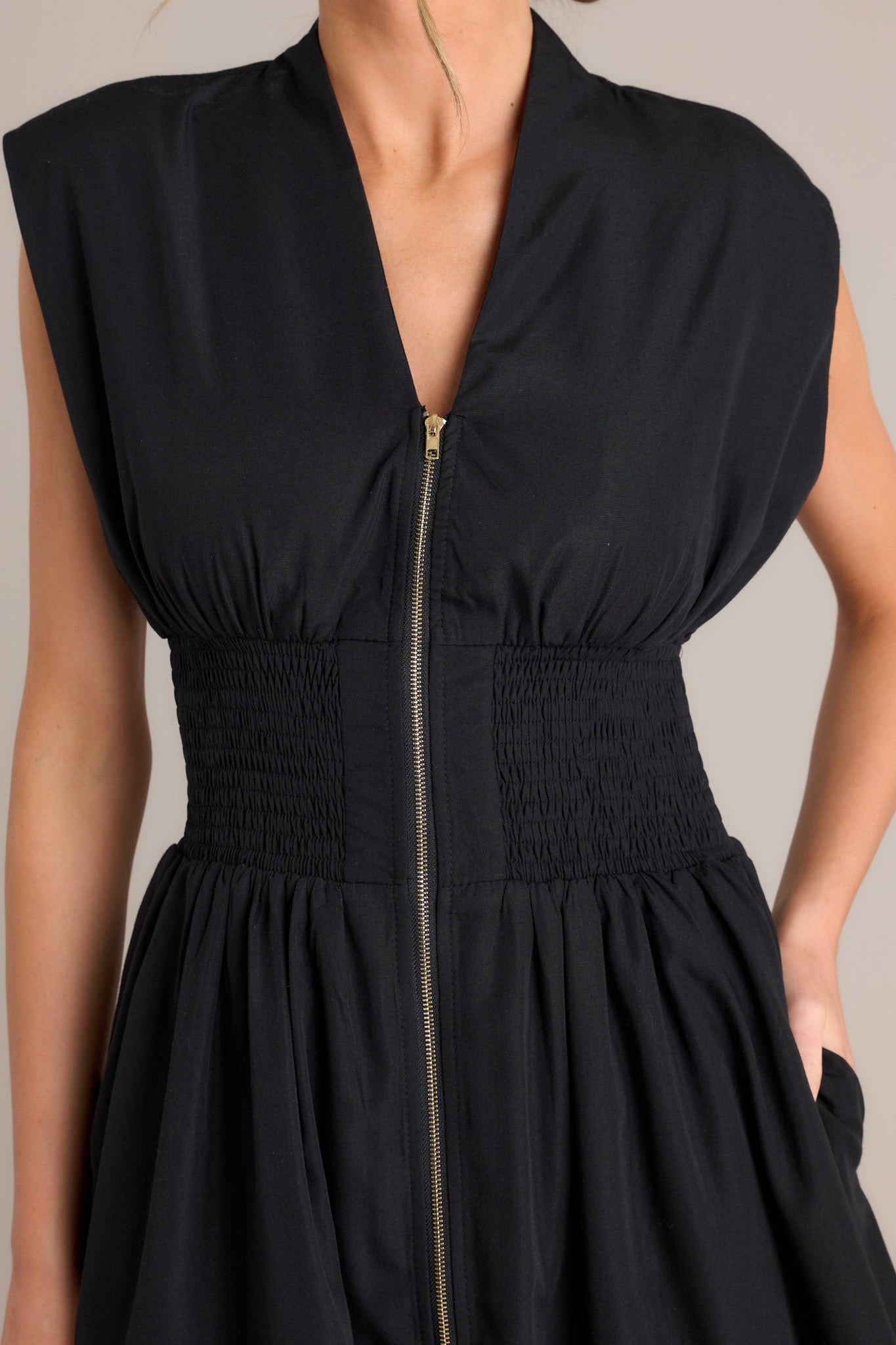 Close-up of the black midi dress showing the v-neckline, padded shoulders, full zipper front, and smocked waist.
