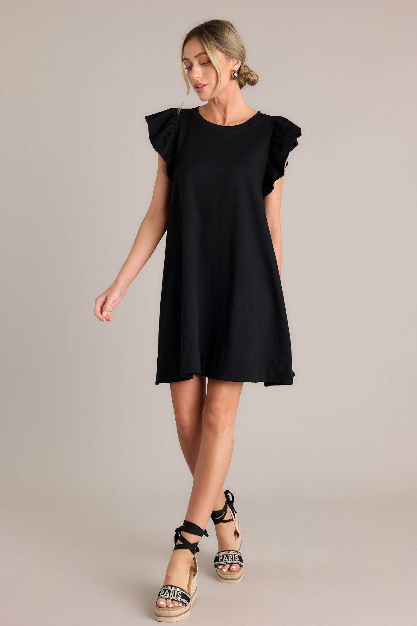 Full length view of a black mini dress with a crew neckline, self-tie drawstring waist feature in the back, functional hip pockets, and ruffled short sleeves