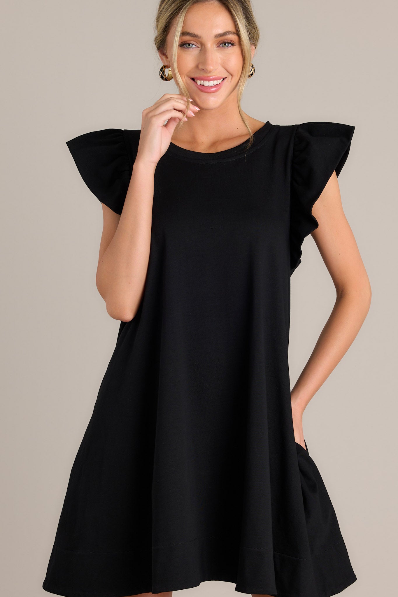 Front view of a black mini dress featuring a crew neckline, functional hip pockets, and ruffled short sleeves.