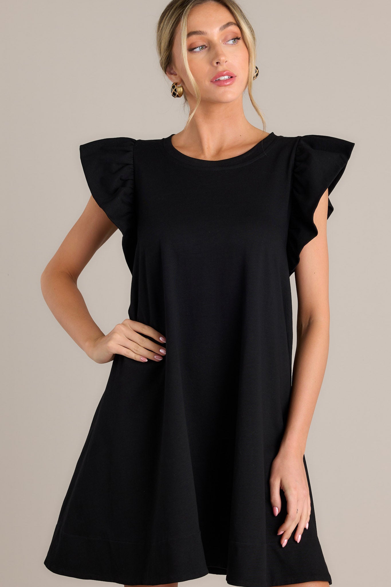 Front angled view of a black mini dress featuring a crew neckline, self-tie drawstring waist feature in the back, functional hip pockets, and ruffled short sleeves