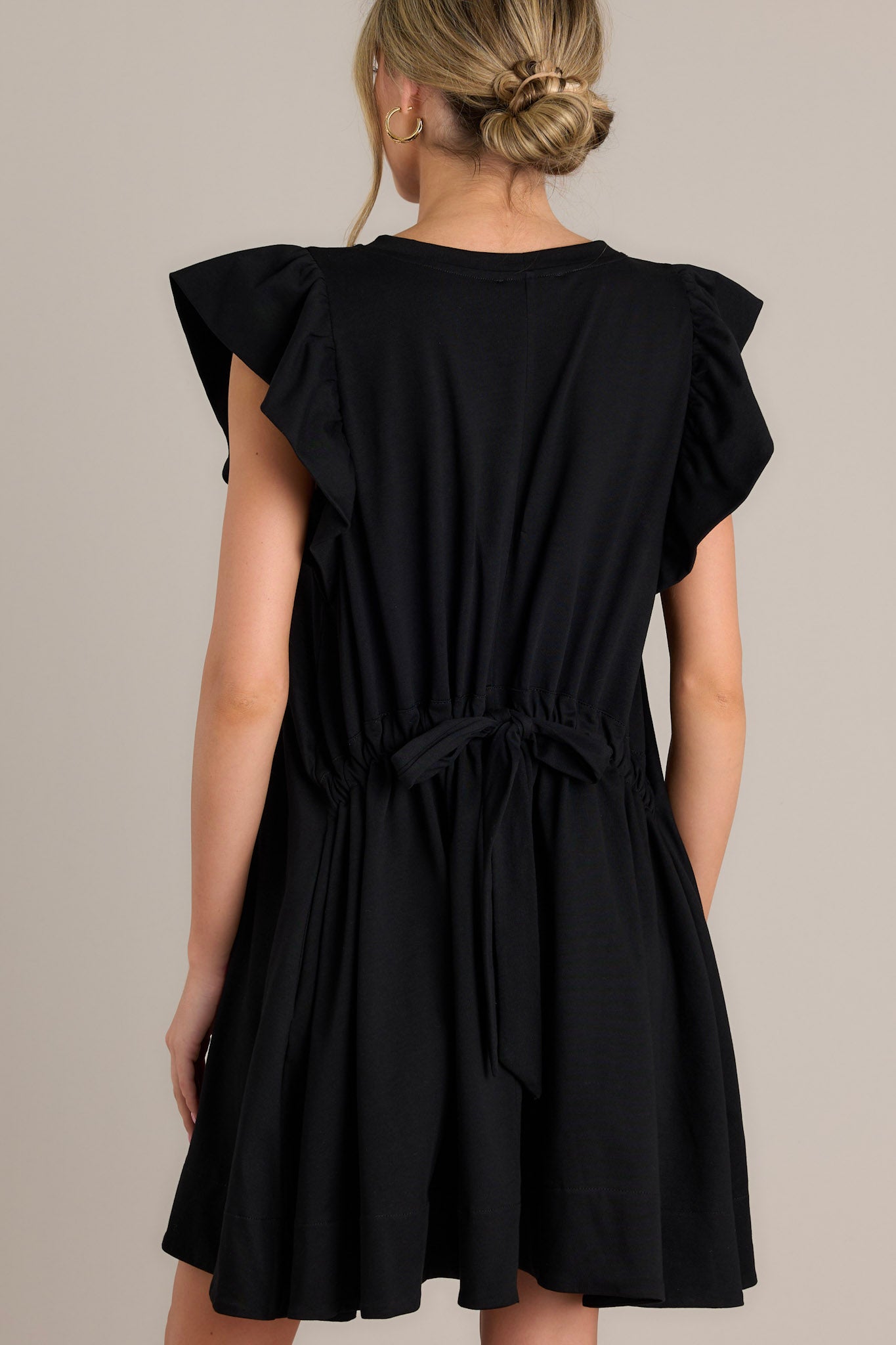 Back view of a black mini dress highlighting the self-tie drawstring waist feature and the overall fit.