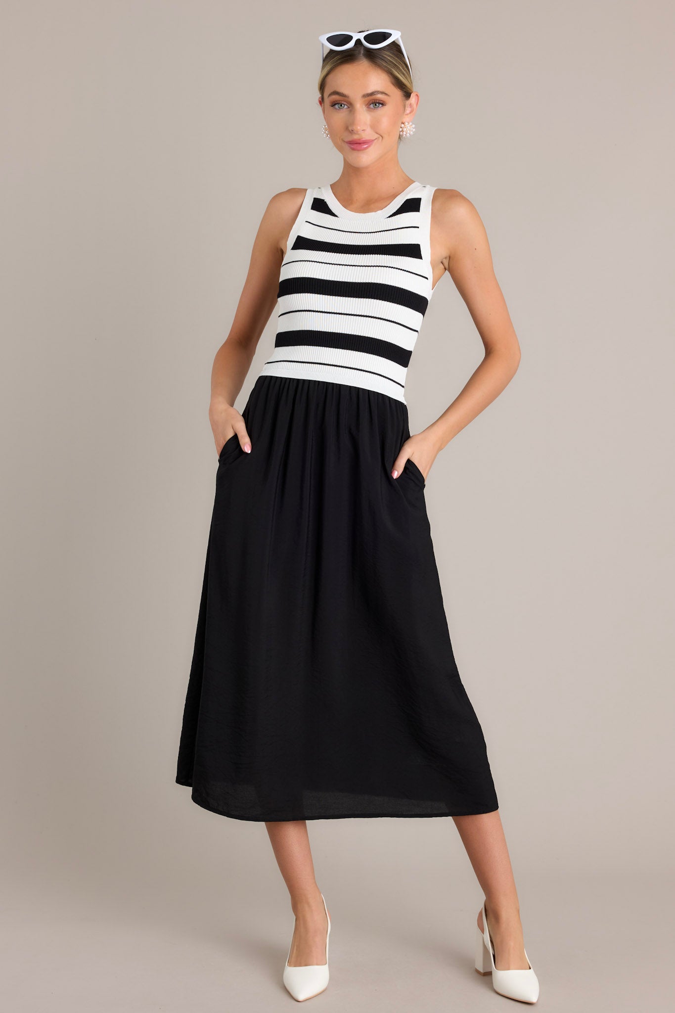 This black striped midi dress features a crew neckline, a striped sweater like bodice, a solid colored skirt, functional hip pockets, and a sleeveless design.