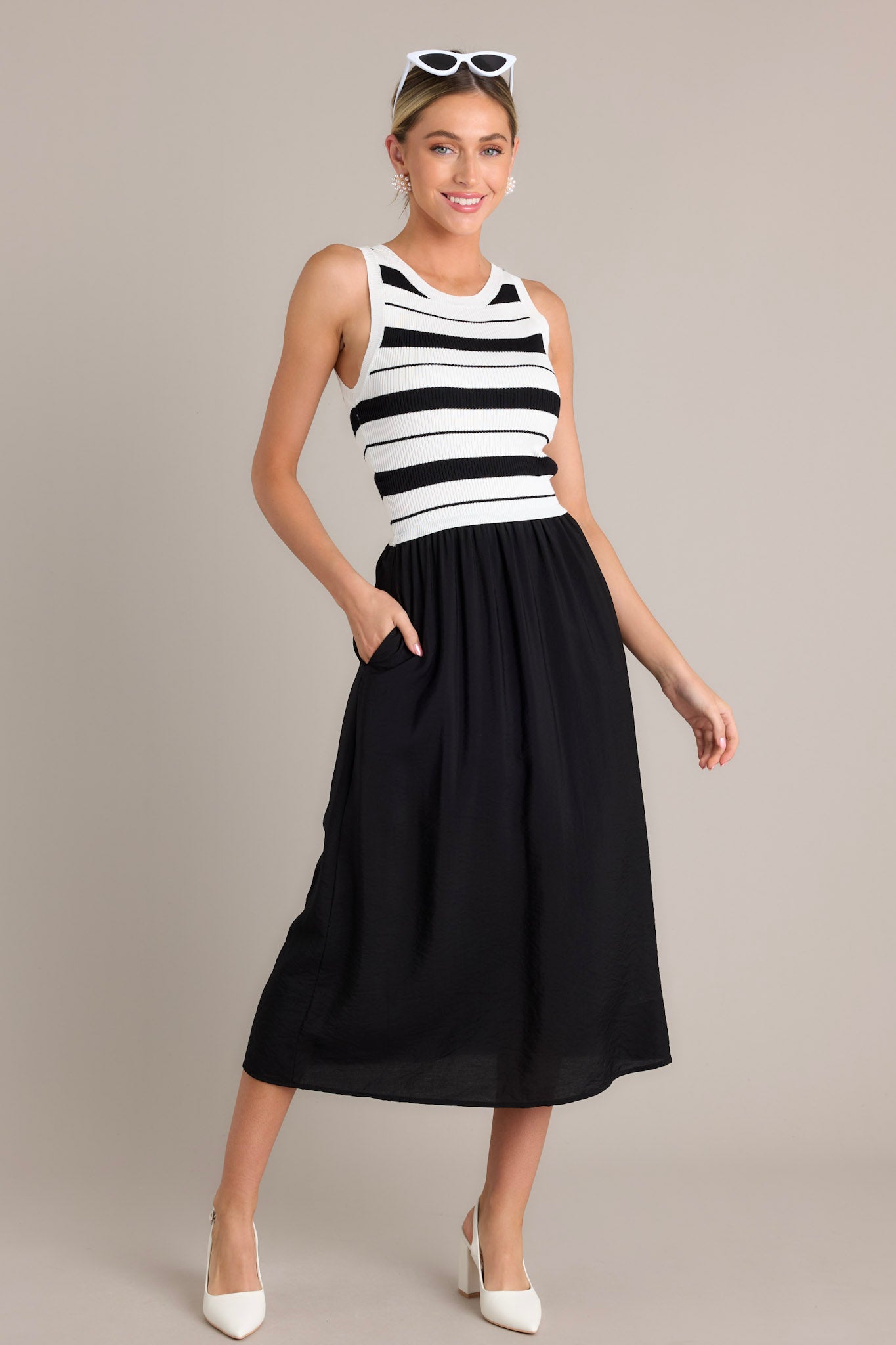 Front angled view of a black striped midi dress featuring a crew neckline, striped sweater-like bodice, solid colored skirt, functional hip pockets, and a sleeveless design