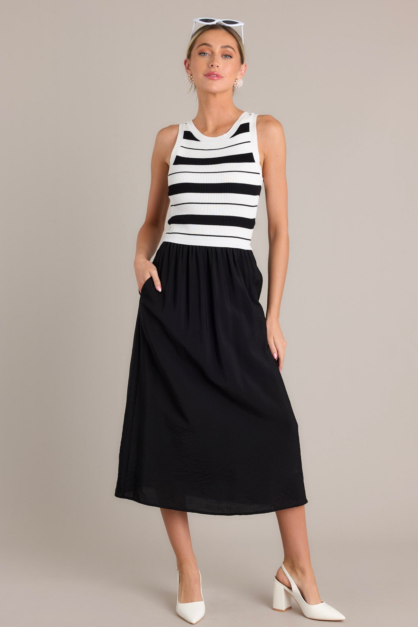 Full length view of a black striped midi dress with a crew neckline, striped sweater-like bodice, solid colored skirt, functional hip pockets, and a sleeveless design