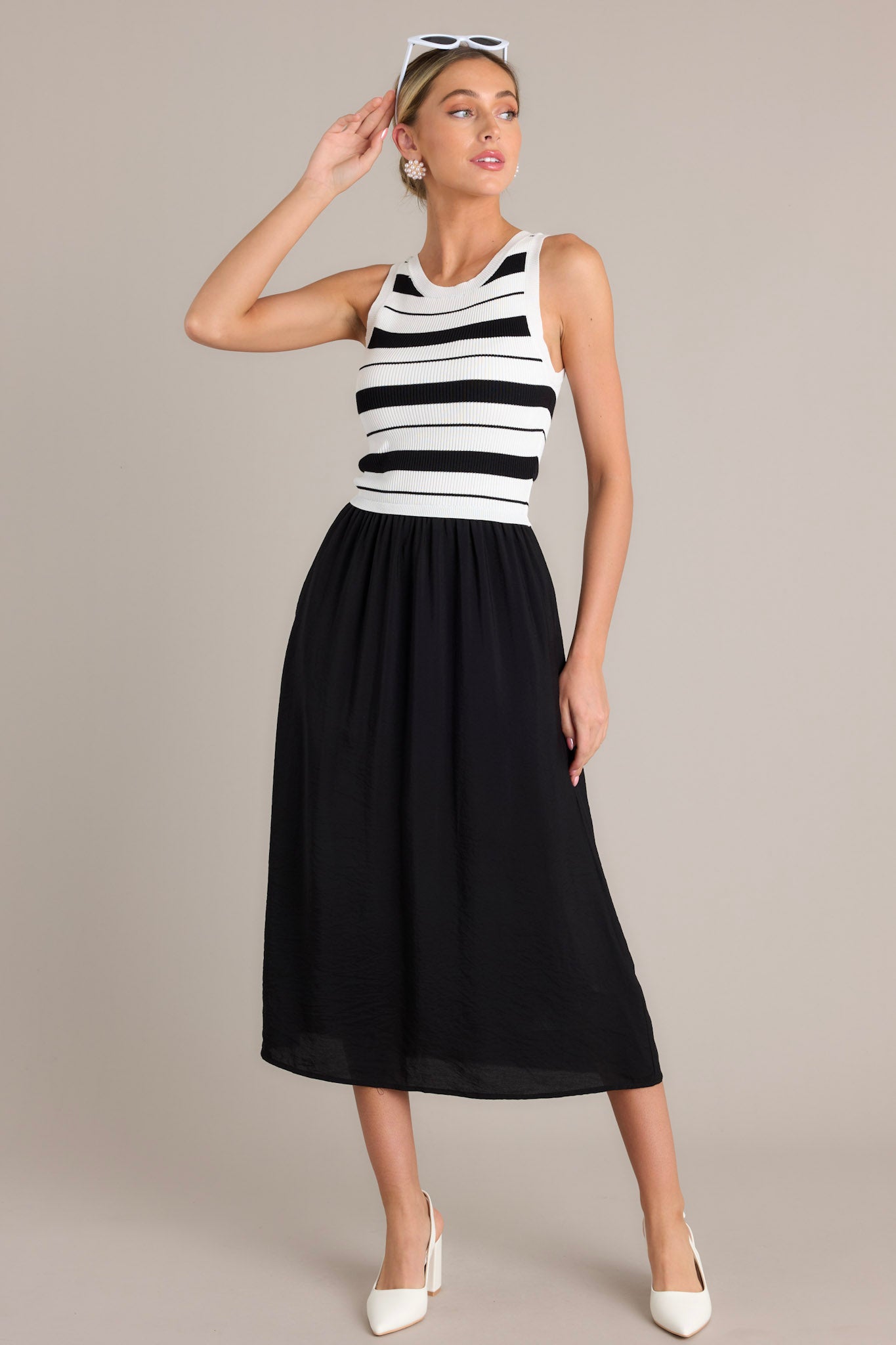 Action shot of a black striped midi dress displaying the fit and movement, highlighting the crew neckline, striped sweater-like bodice, solid colored skirt, functional hip pockets, and sleeveless design.