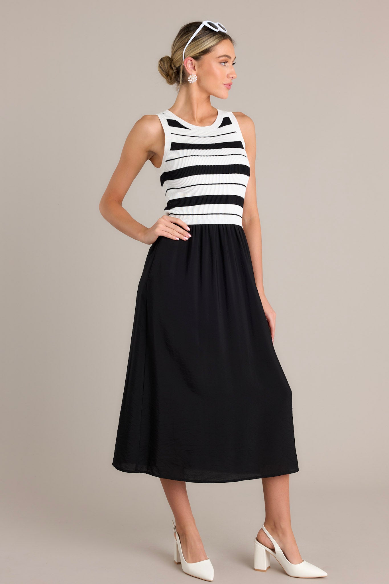 Side view of a black striped midi dress showcasing the crew neckline, striped sweater-like bodice, solid colored skirt, functional hip pockets, and sleeveless design.
