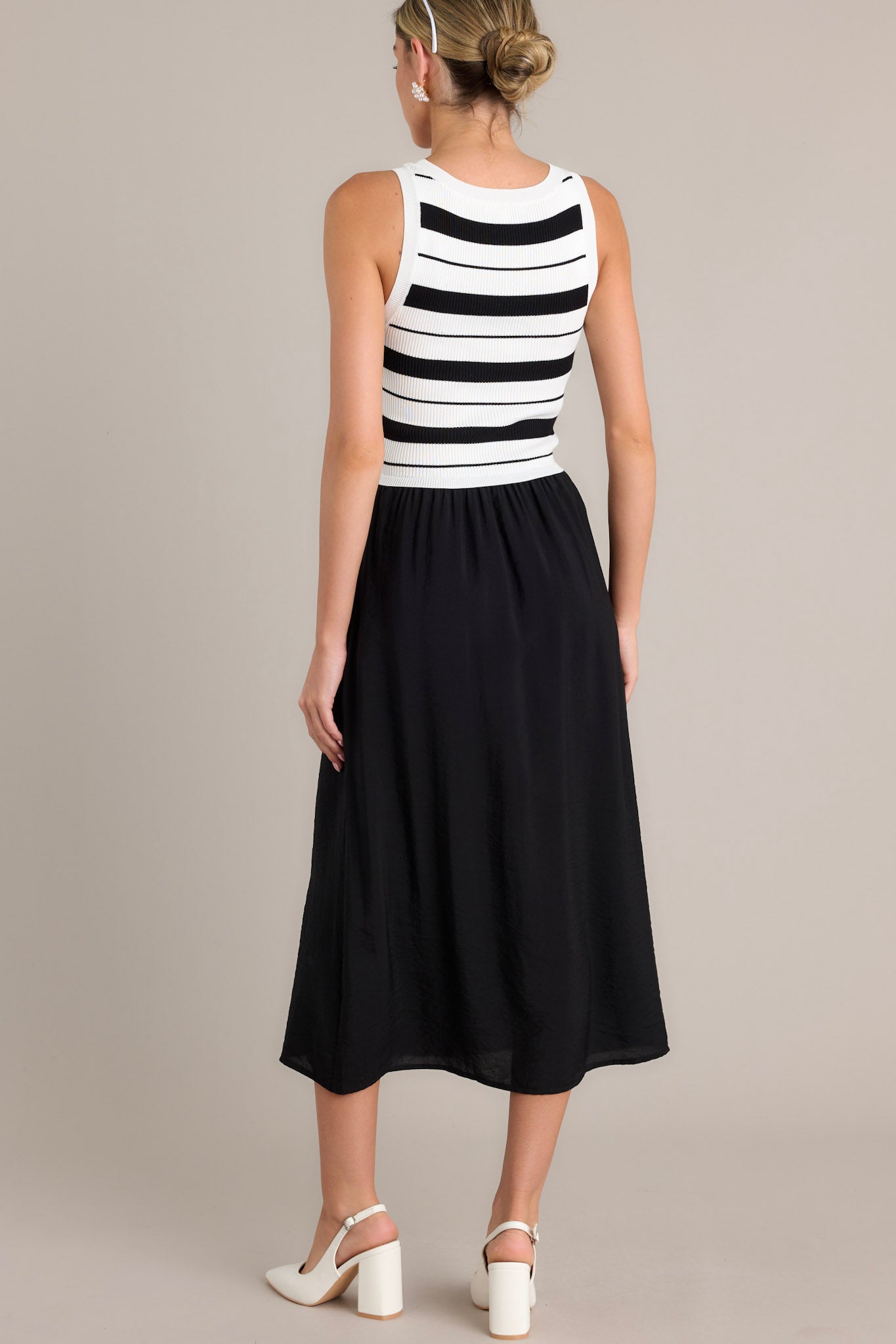 Back view of a black striped midi dress highlighting the striped sweater-like bodice, solid colored skirt, and sleeveless design.