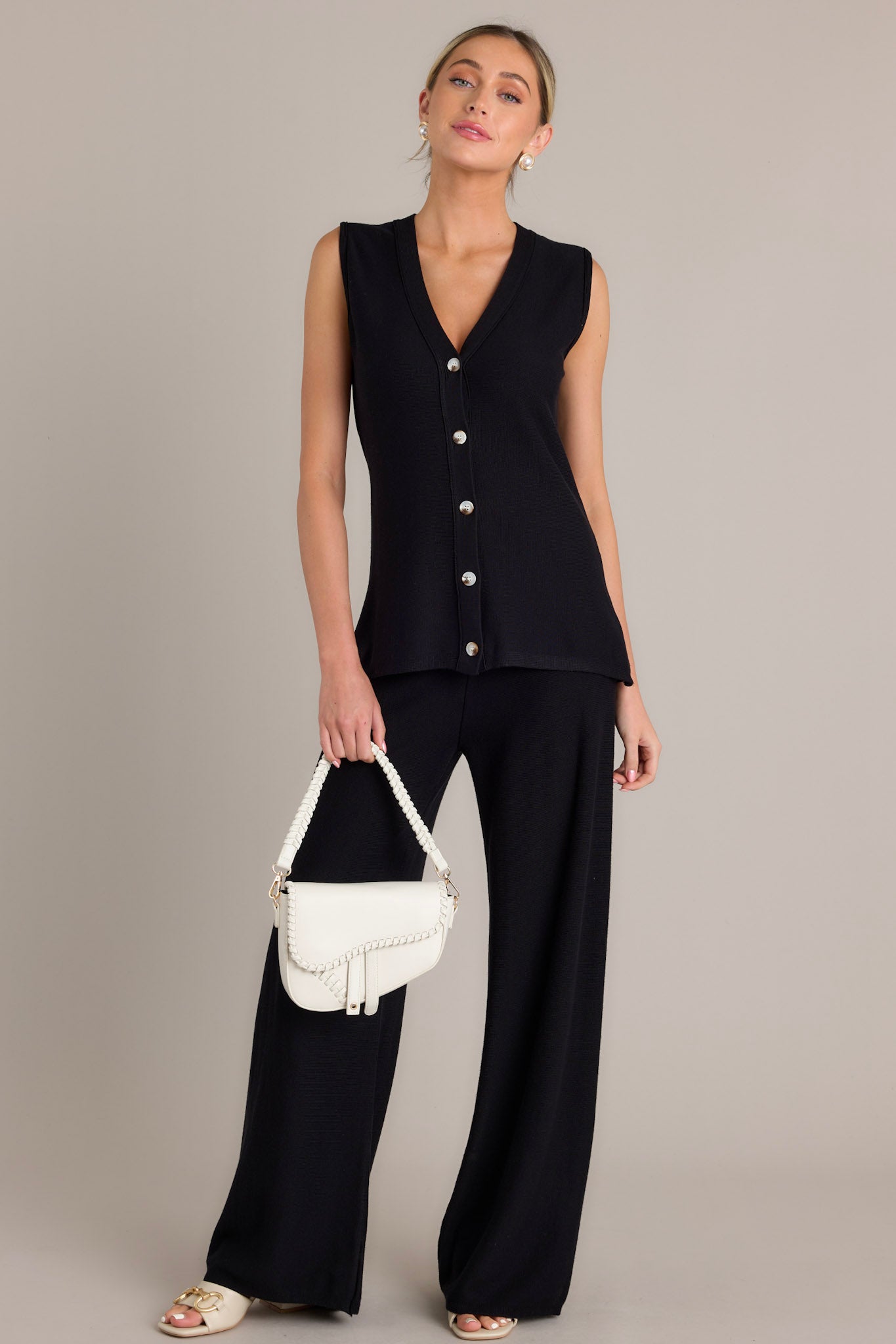 This black sleeveless top features functional buttons down the front, and a lightweight knit fabric. 