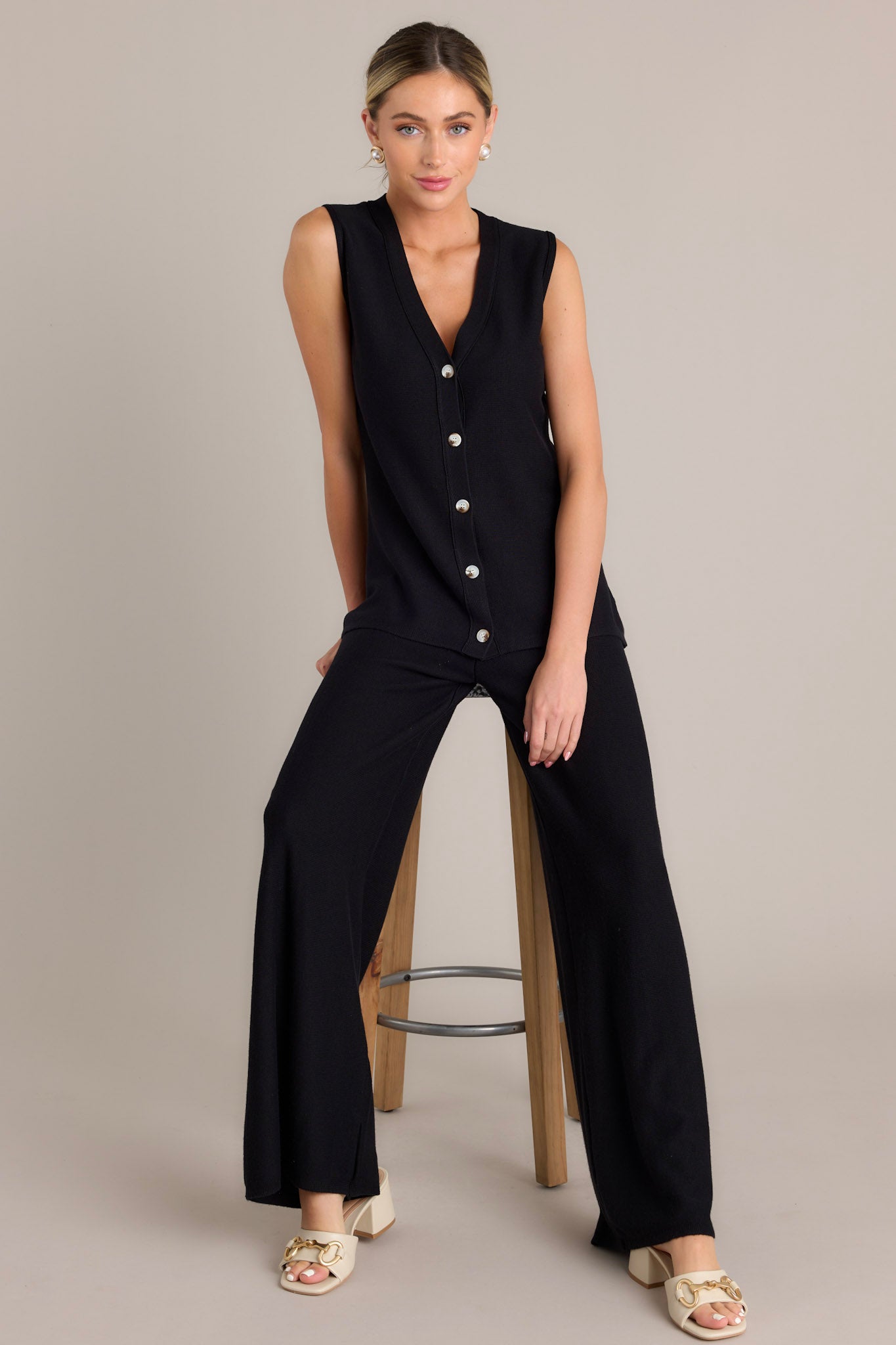 Full body view of this black sleeveless top featuring a v-neckline and functional buttons. 