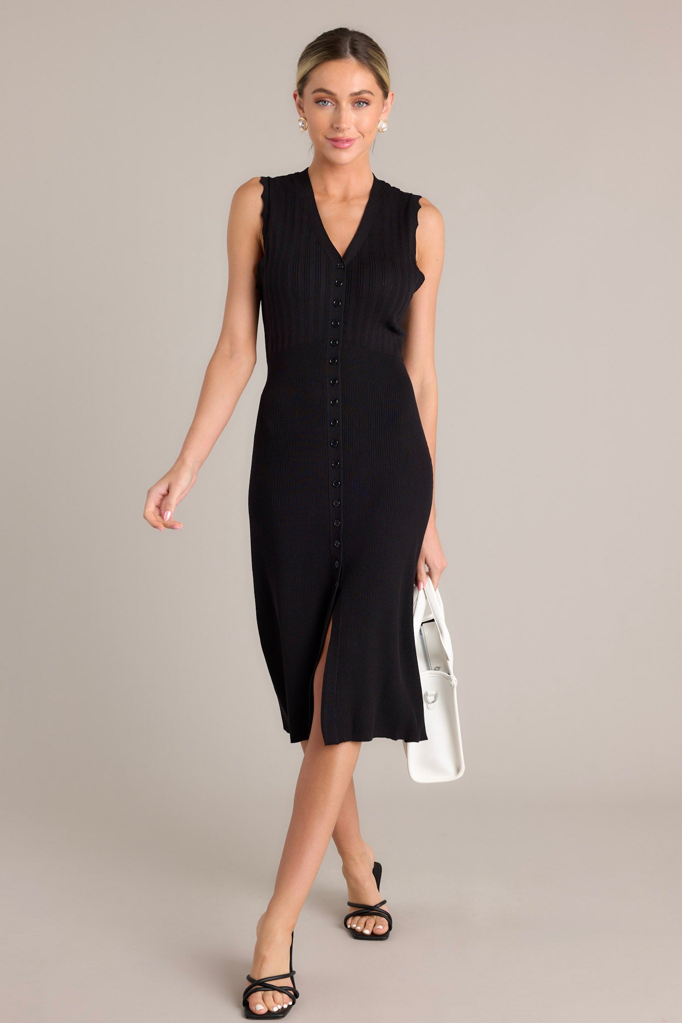 Full length view of a black dress with a v-neckline, a functional button front, a front slit, and scalloped sleeves