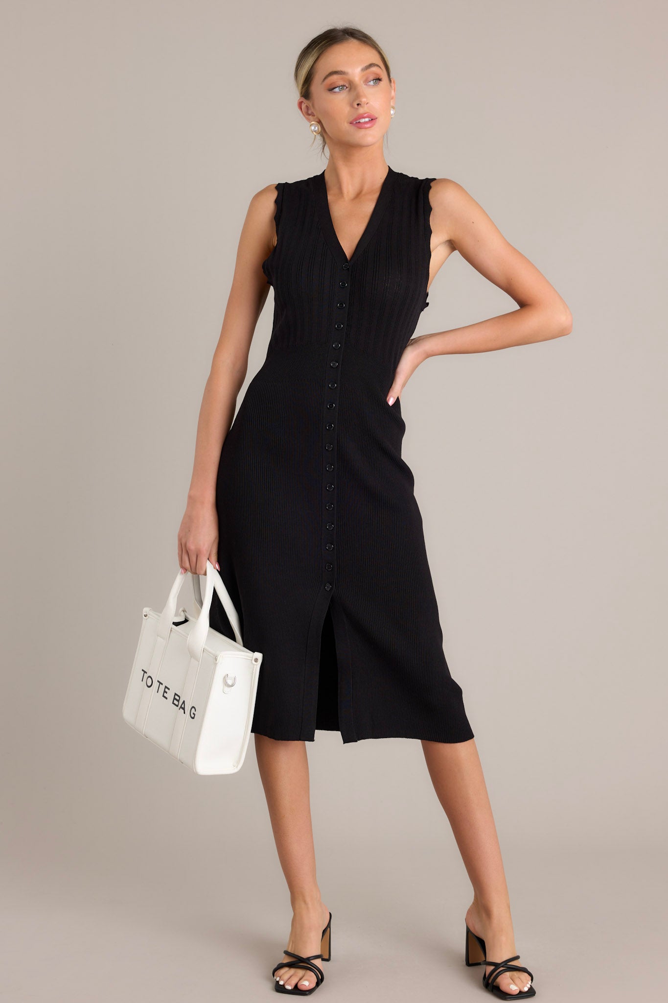 This black dress features a v-neckline, a functional button front, a front slit, and scalloped sleeves.