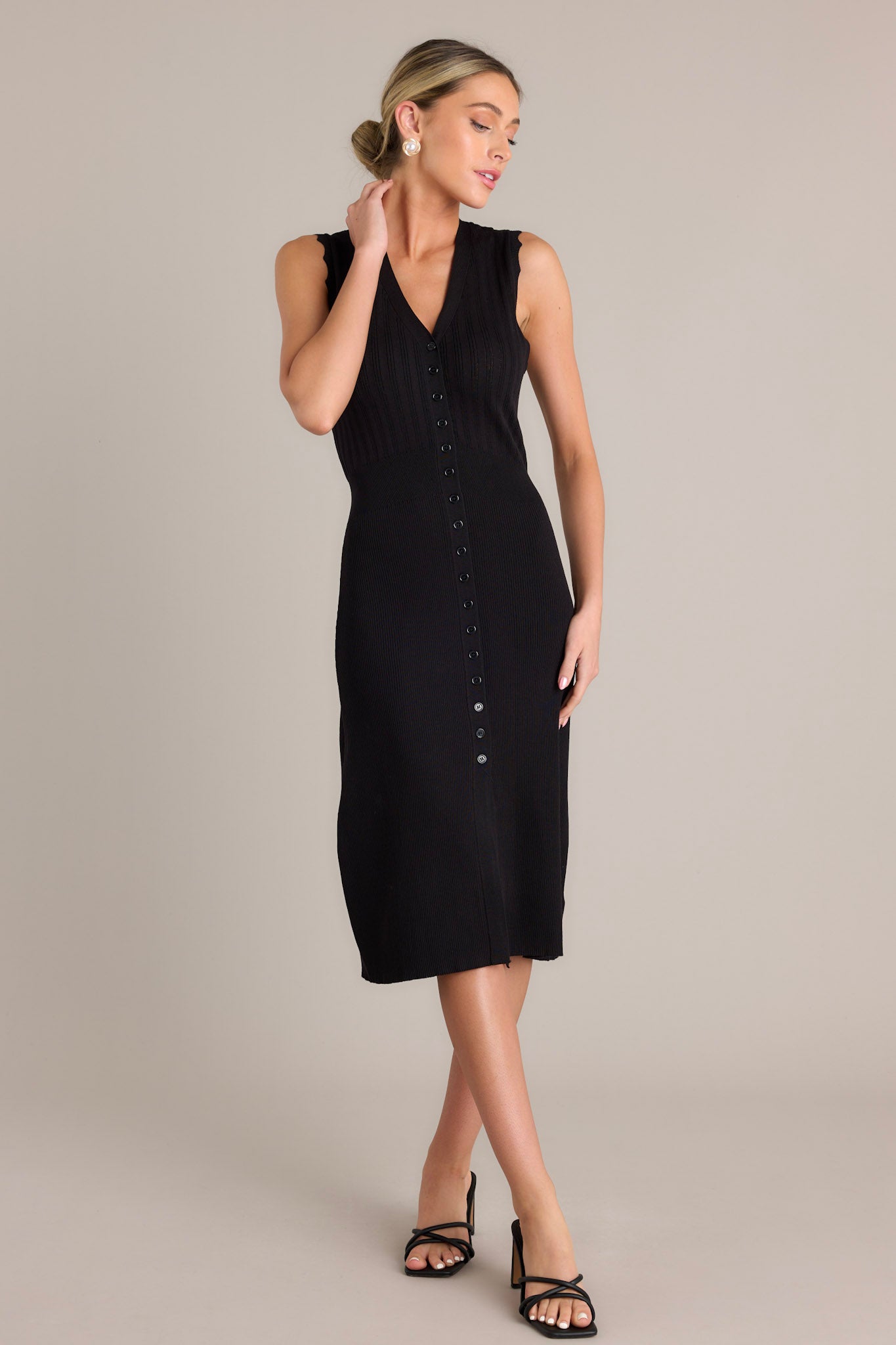 Front angled view of a black dress featuring a v-neckline, a functional button front, a front slit, and scalloped sleeves