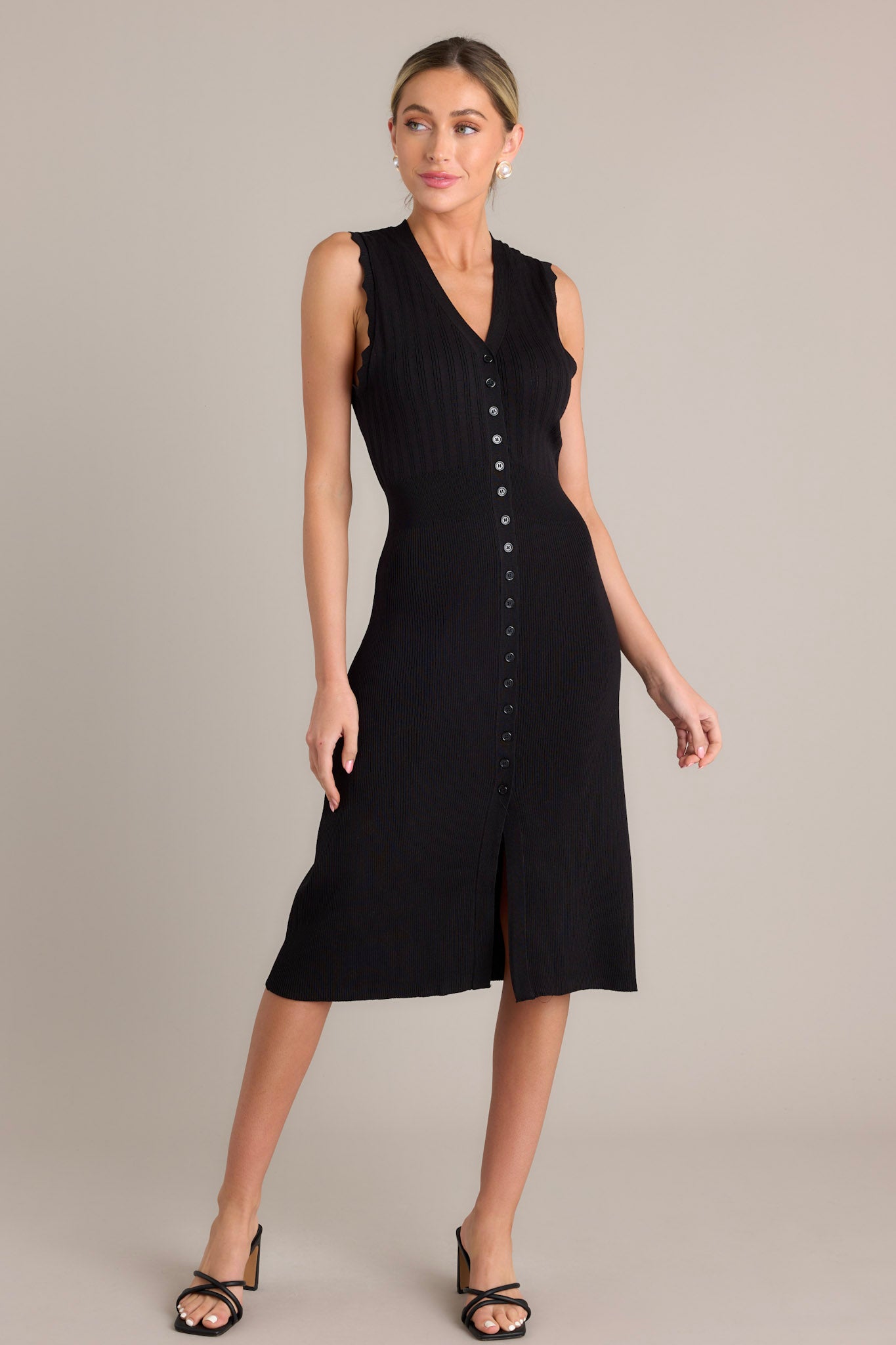 Action shot of a black dress displaying the fit and movement, highlighting the v-neckline, functional button front, front slit, and scalloped sleeves.