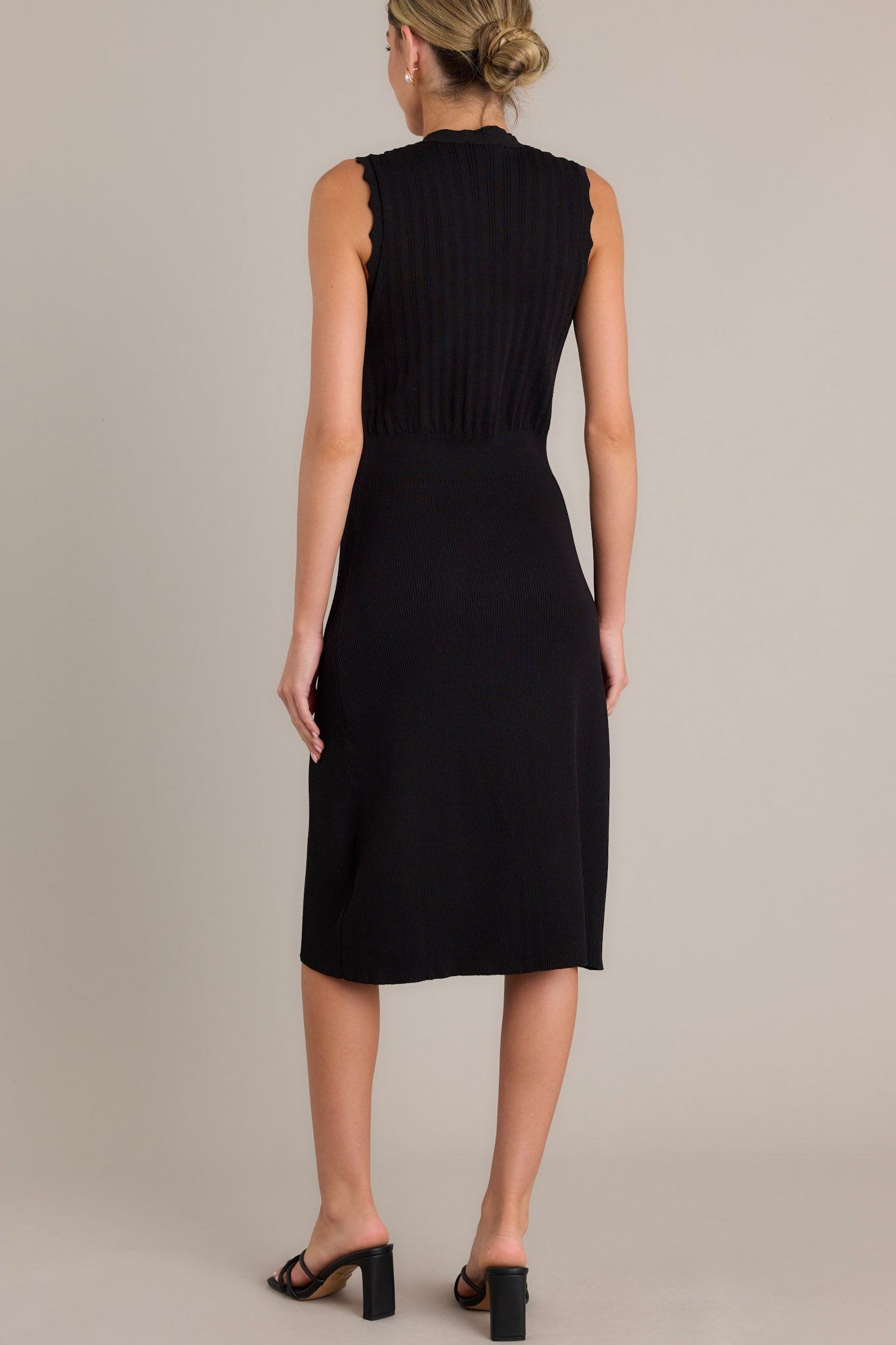 Back view of a black dress highlighting the overall fit and the scalloped sleeves.