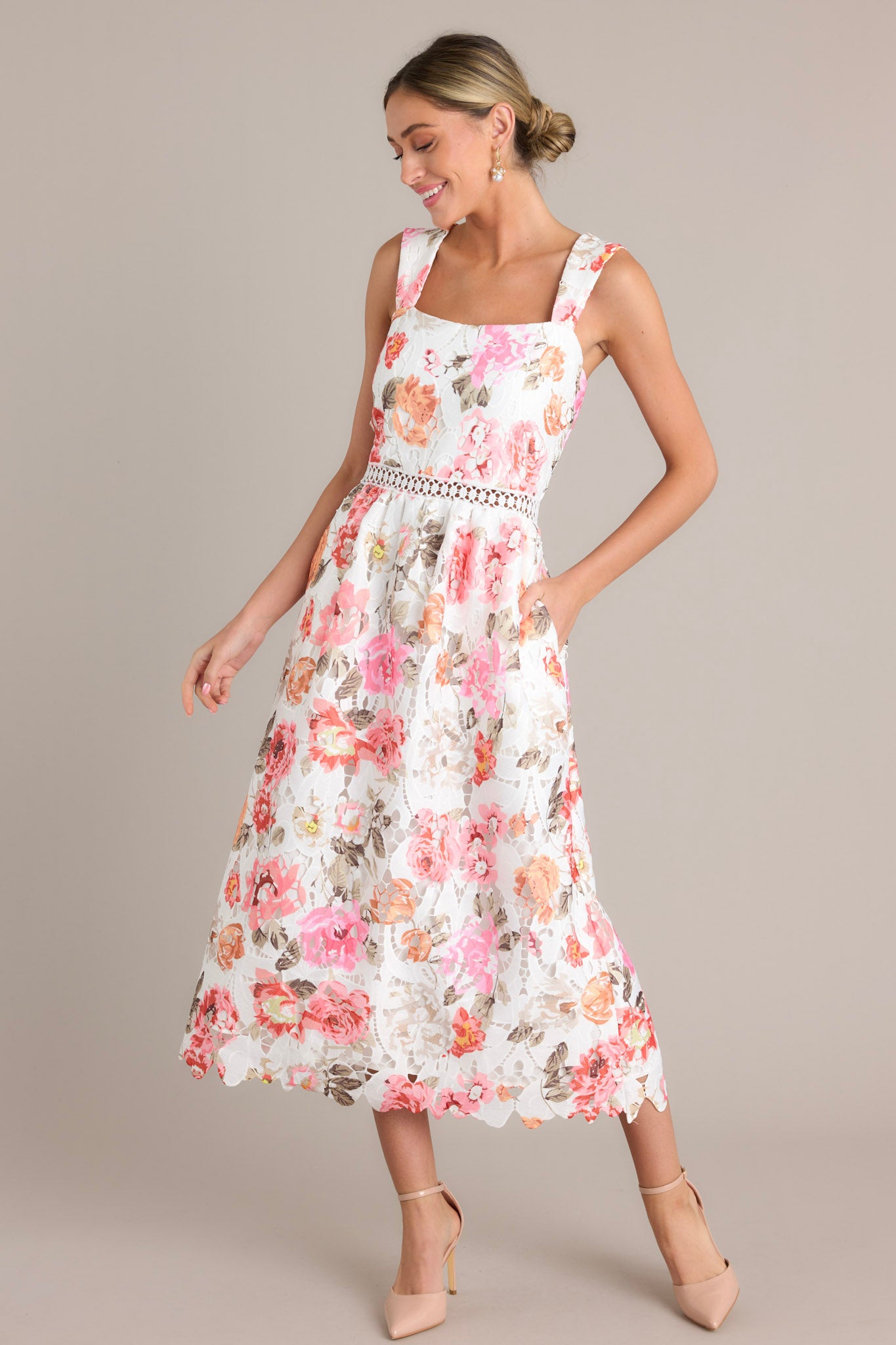 White multi floral midi dress with a square neckline, fitted bodice, crocheted cinched waist, and functional pockets, showcasing a full lace skirt that reaches mid-length.