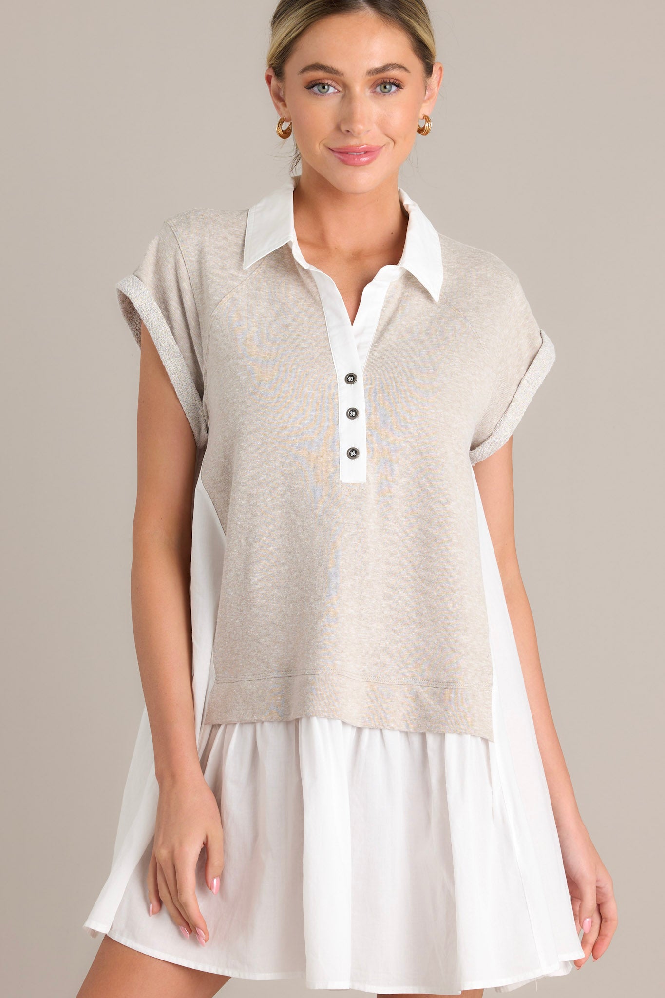 Front angled view of a taupe mini dress featuring a collared v-neckline, functional chest buttons, an attached sweater overlay, and cuffed short sleeves