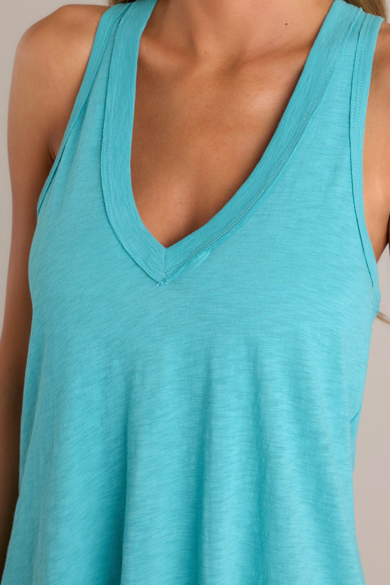 Close-up of the v-neckline and racerback design of a teal mini dress, highlighting the flowing silhouette and summer-ready color.