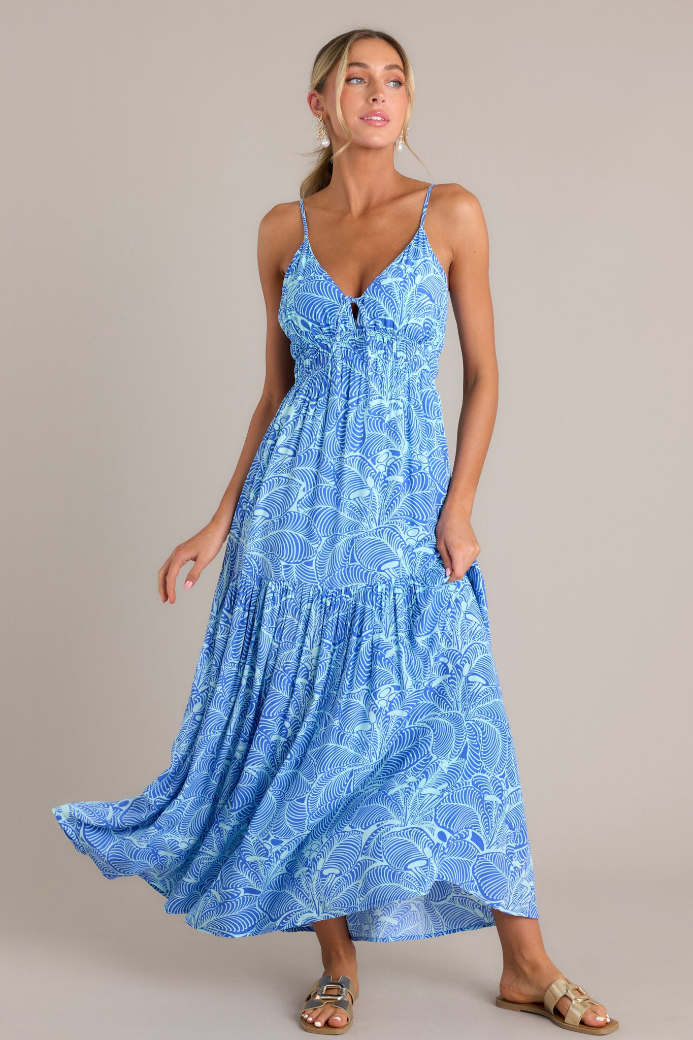 Featuring a v-neckline, thin adjustable straps, and a self-tie bust, this blue maxi dress also has an elastic waistband and a tiered, flowing silhouette.