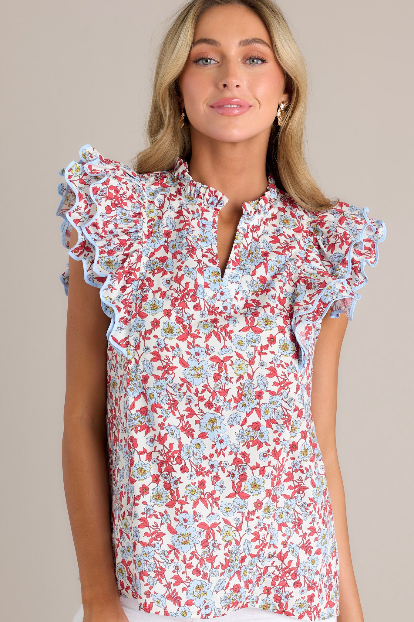 Front view of a red top featuring a ruffled v-neckline, a red & light blue floral print, and ruffled short sleeves with ricrac detailing.