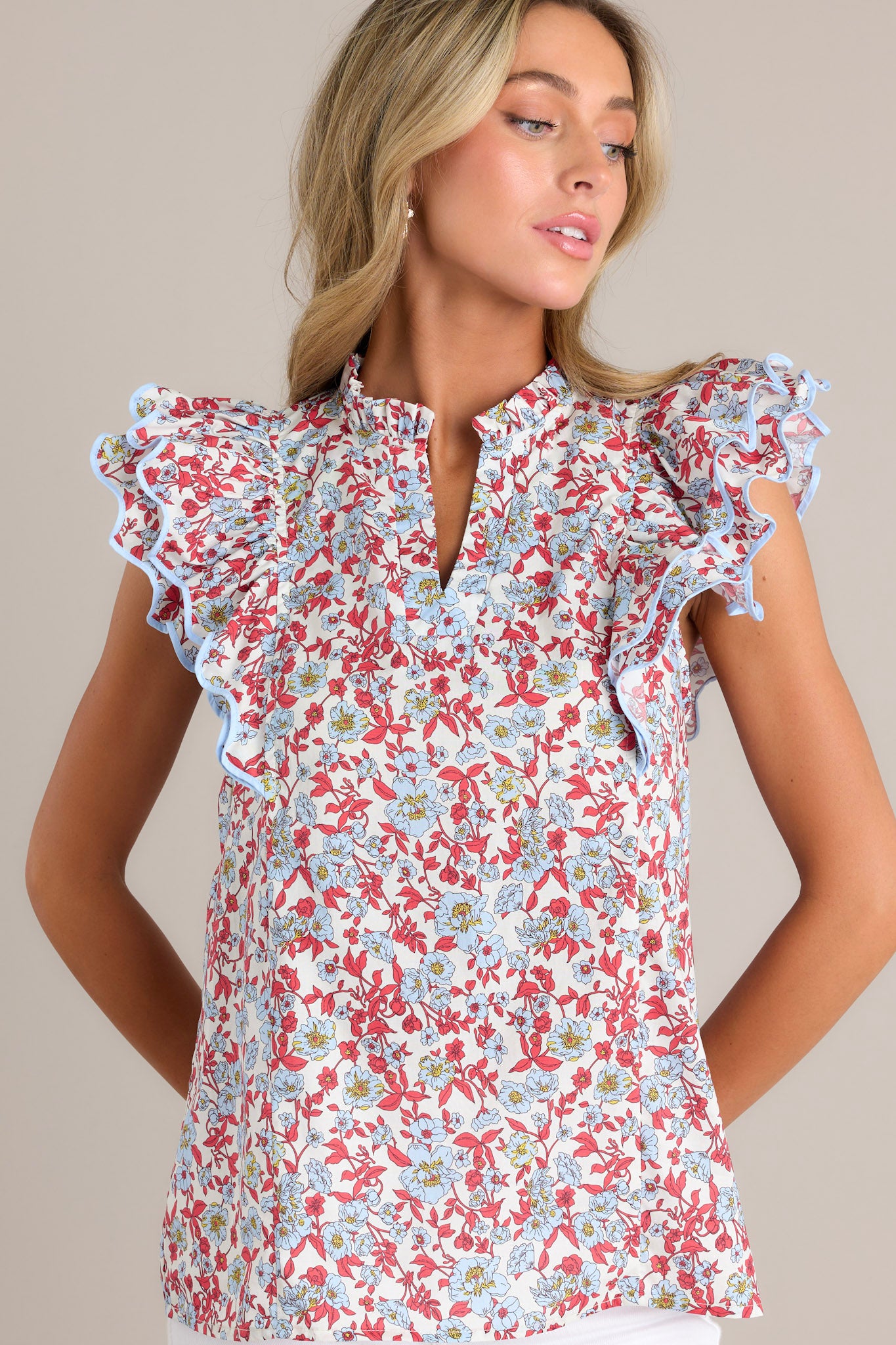 A detailed close-up of the red top highlighting the intricate ruffled v-neckline, the vibrant red & light blue floral print, and the ricrac trim on the short sleeves.