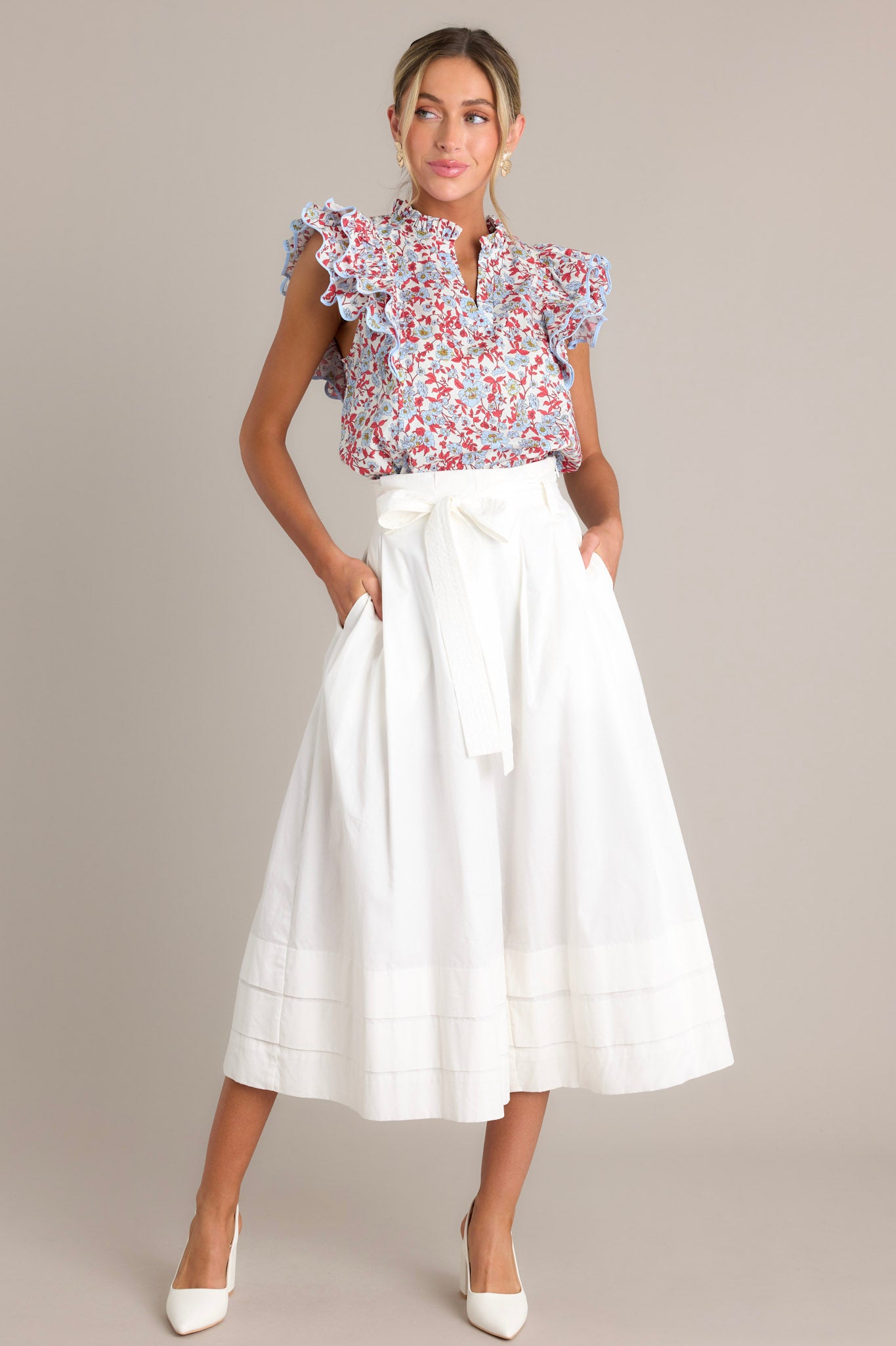 Full length view of a red top featuring a ruffled v-neckline, a red & light blue floral print, and ruffled short sleeves with ricrac detailing.