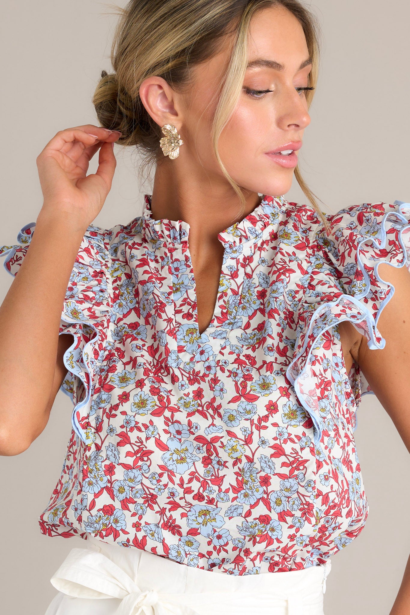 Front angled view of a red top featuring a ruffled v-neckline, a red & light blue floral print, and ruffled short sleeves with ricrac detailing.