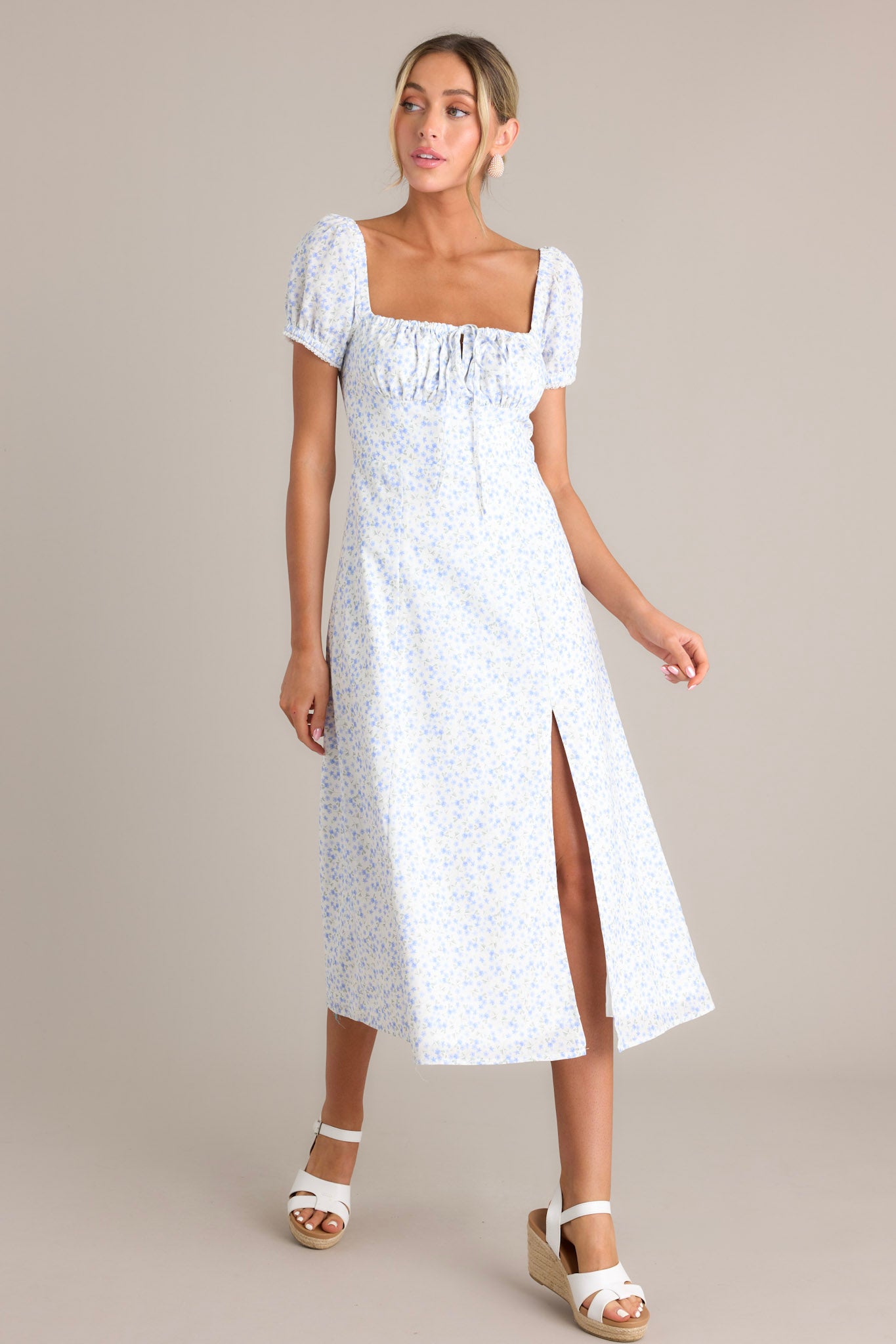 This blue midi dress features small blue flowers on a white background, puff sleeves, and a ruched bust, showcasing a front slit.