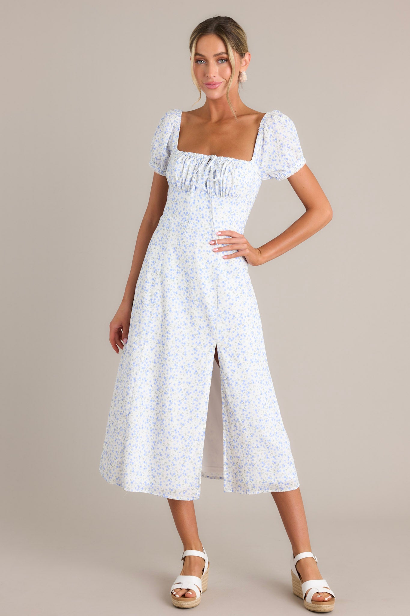 Blue midi dress with delicate blue floral print, puff sleeves, square neckline, and front slit, highlighted by a fitted waist and ruched bust.