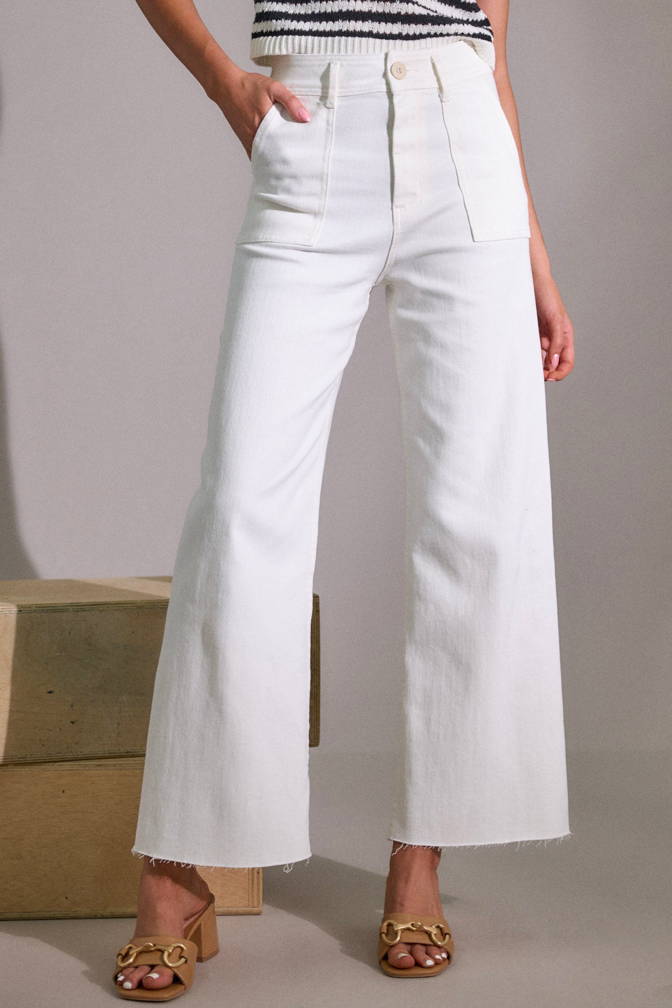 Front angled view of white jeans featuring a high waisted design, a classic button & zipper closure, belt loops, functional front & back pockets, a wide leg design, and a raw hemline.