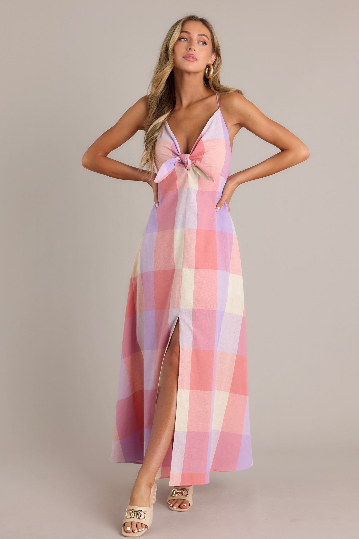 Action shot of a pink maxi dress with a v-neckline, self-tie bust feature, thin self-tie straps, an open back, a discrete back zipper, a large plaid pattern, and a 22.5" front slit, highlighting the dress's flow and movement.