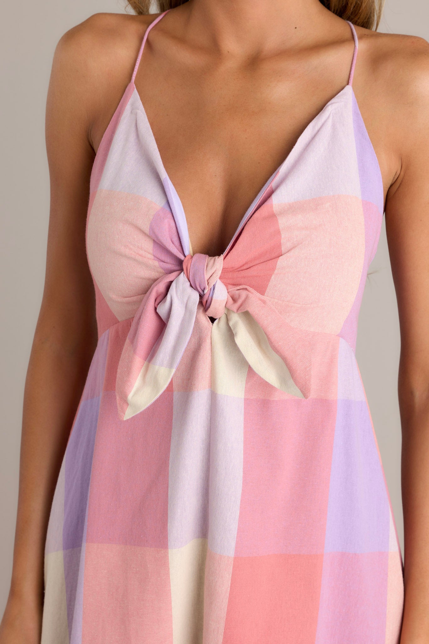 Close-up of the v-neckline, self-tie bust feature, thin self-tie straps, and plaid pattern of a pink maxi dress.