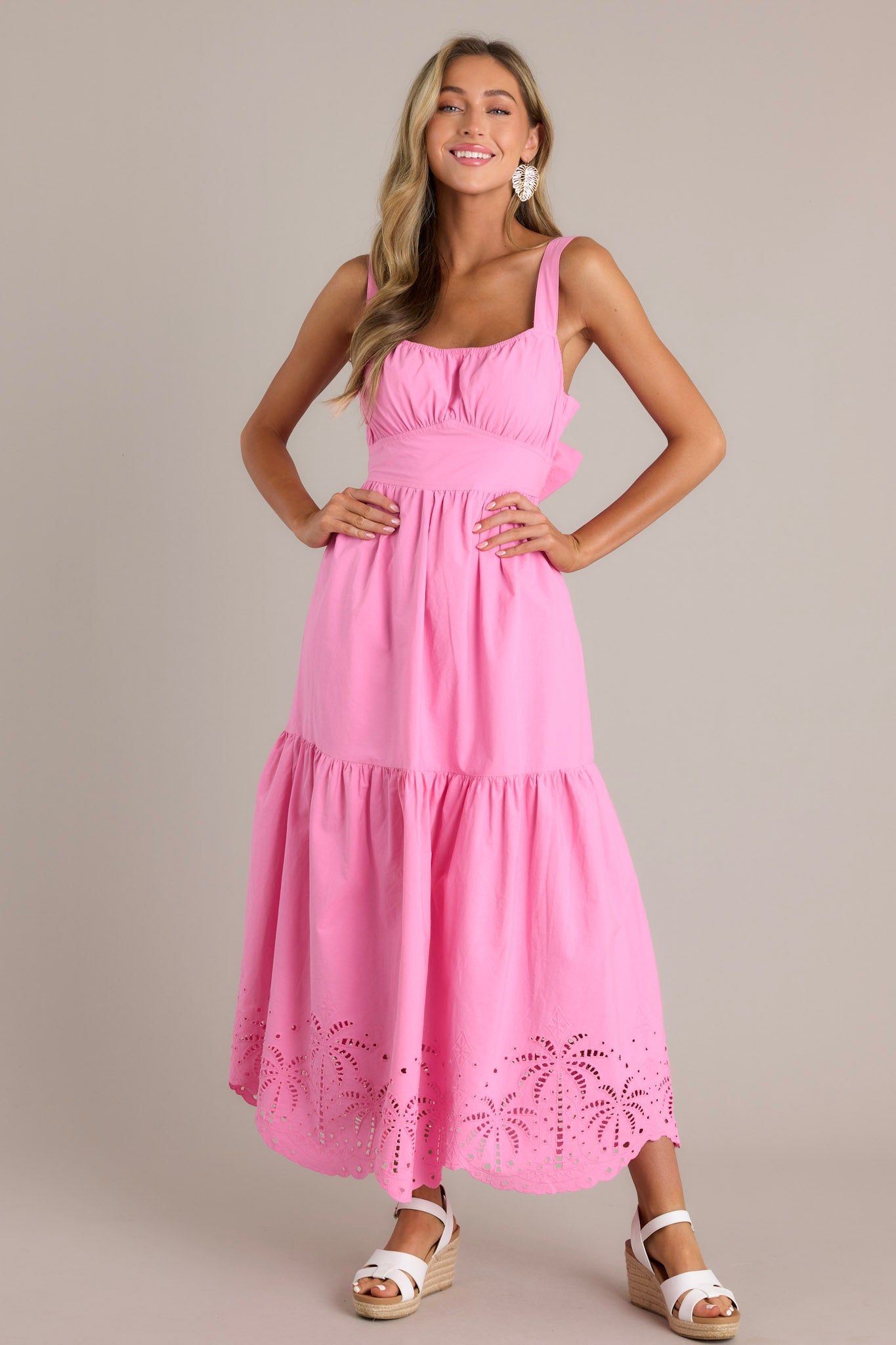 Front view of a pink midi dress featuring an elastic square neckline, thick adjustable straps, a thick waistband with a self-tie back feature, an open lower back, a single tier, palm eyelet detailing, and a scalloped hemline.
