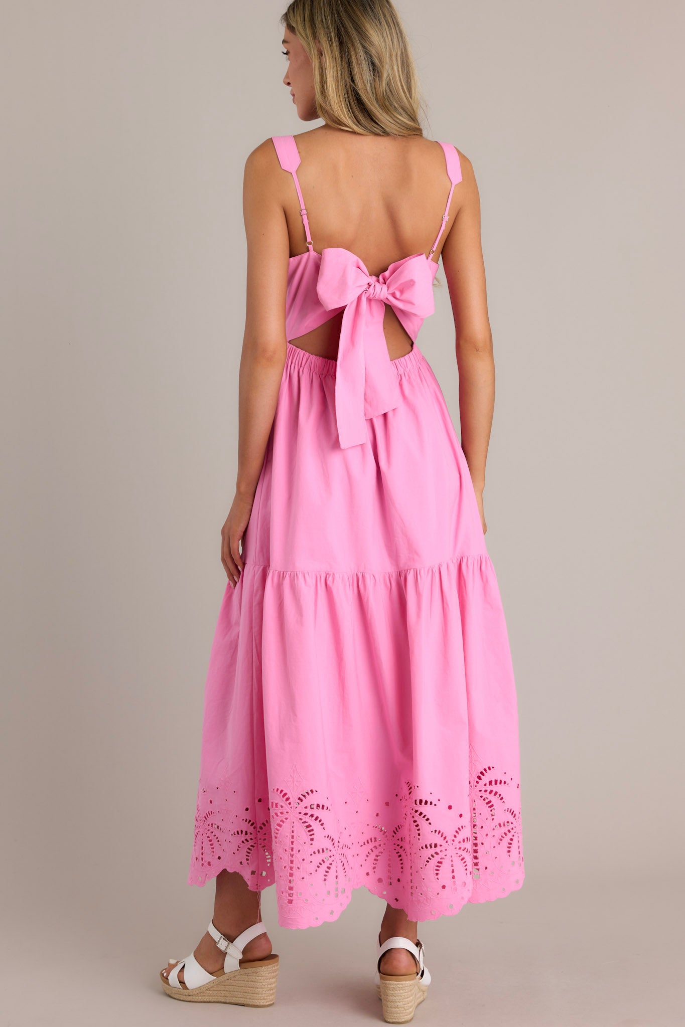 Back view of a pink midi dress highlighting the self-tie back feature, open lower back, and the palm eyelet detailing on the scalloped hemline.
