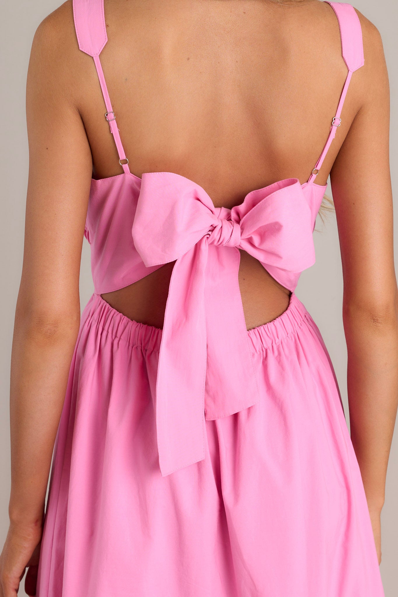 Close-up view of the back of this pink midi dress that features an open back and a self-tie back feature.