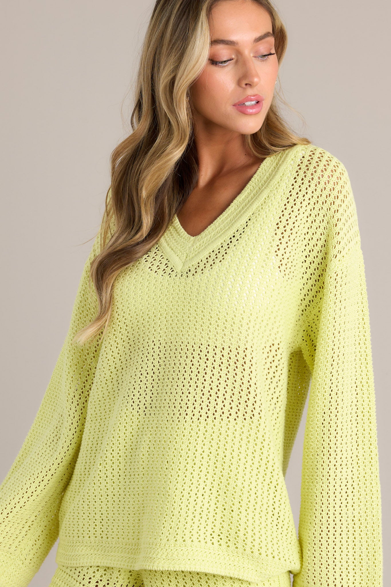 Side view of a lime sweater showcasing the v-neckline, relaxed fit, open knit design, and wide long sleeves.