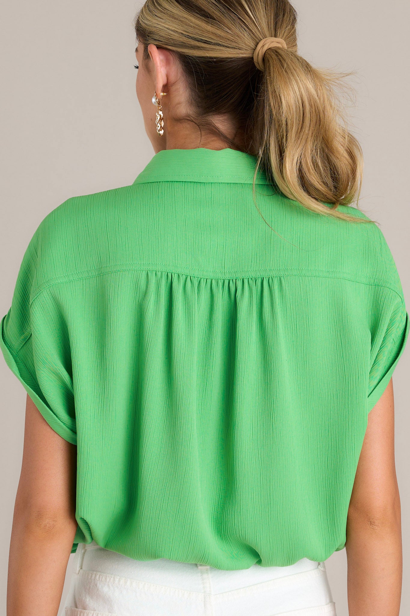 Back view of a green top highlighting the relaxed fit, cuffed short sleeves, and self-tie drawstring hemline.