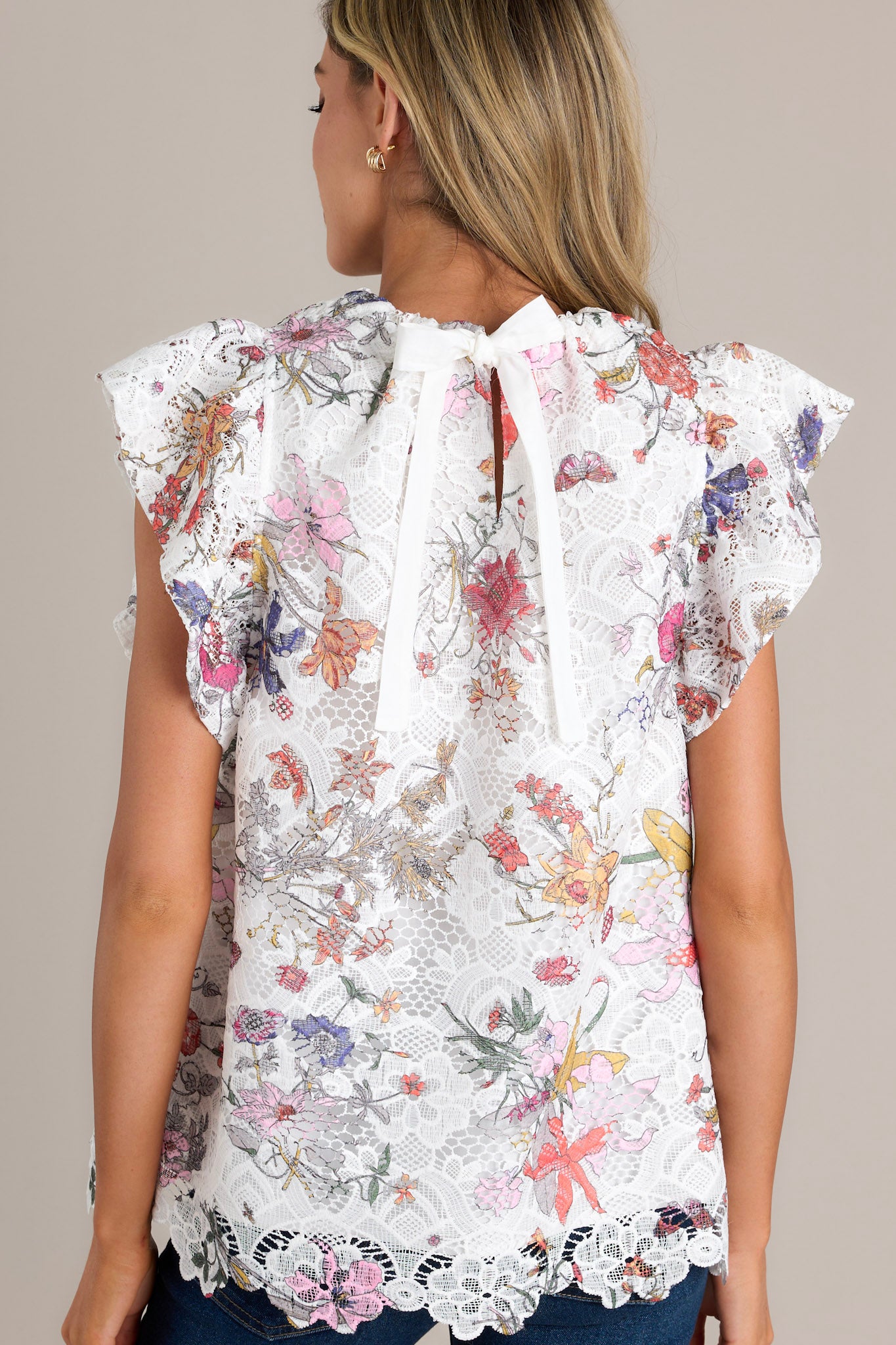 Back view of a white top highlighting the self-tie feature at the back of the neck, floral lace overlay, and ruffled short sleeves.