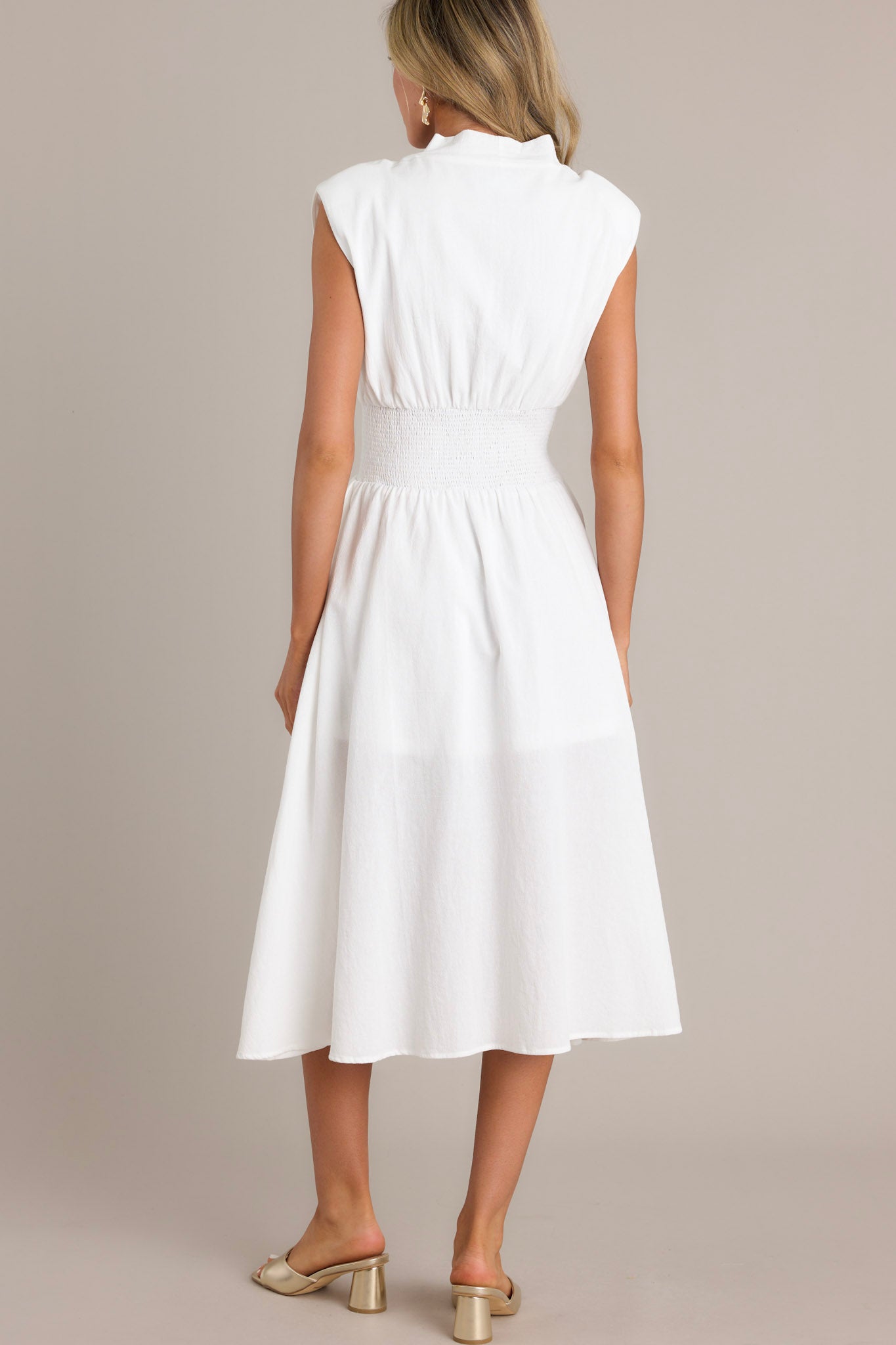 Back view of a white midi dress featuring a plain design, showing the shoulder padding and flowing silhouette.