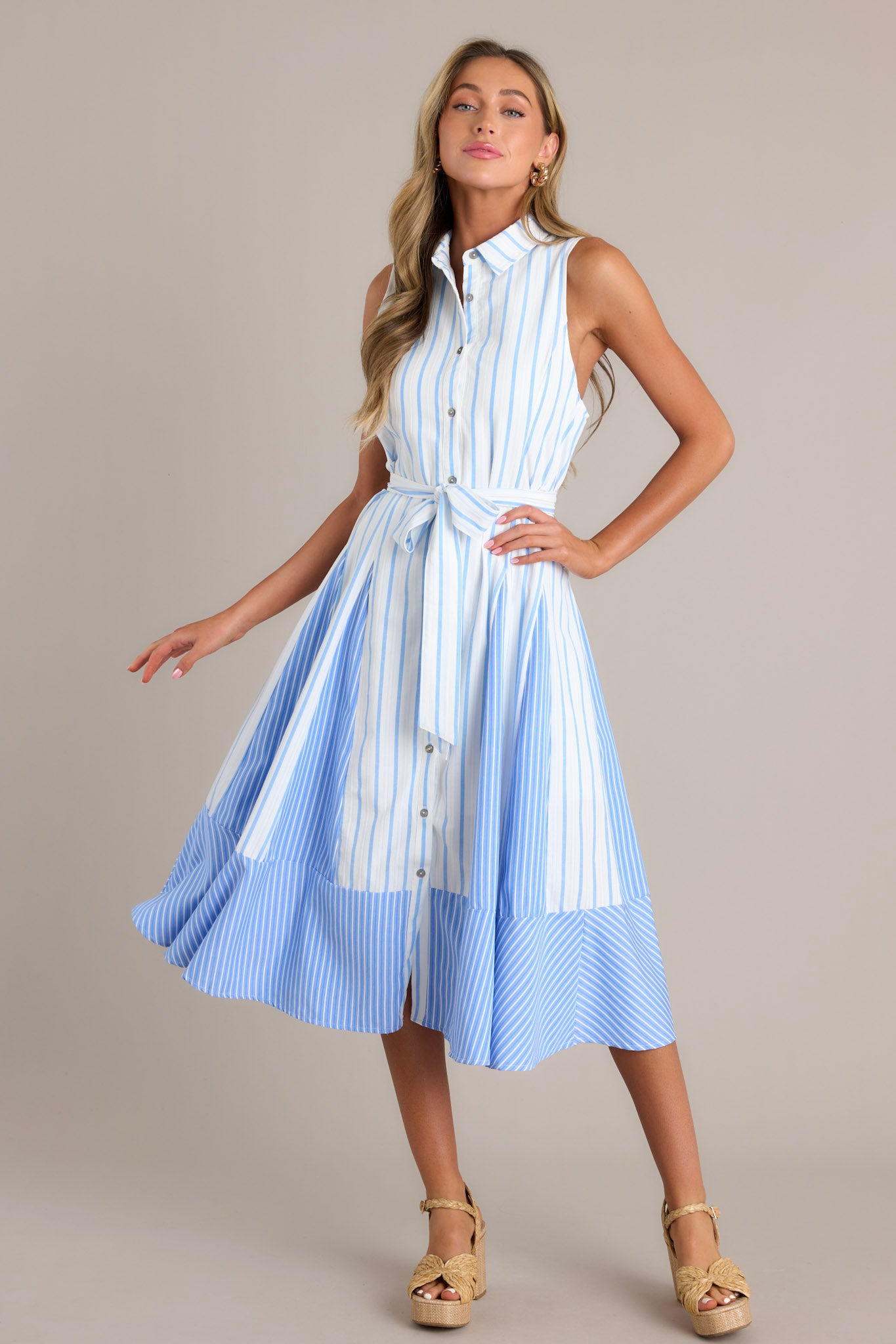 Full length view of a light blue midi dress featuring a collared neckline, a functional button front, a self-tie waist belt, a unique stripe pattern, and a flowing silhouette