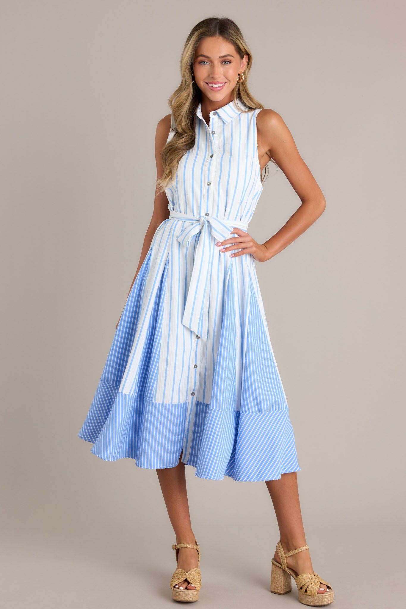 This light blue midi dress features a collared neckline, a functional button front, a self-tie waist belt, a unique stripe pattern, and a flowing silhouette.