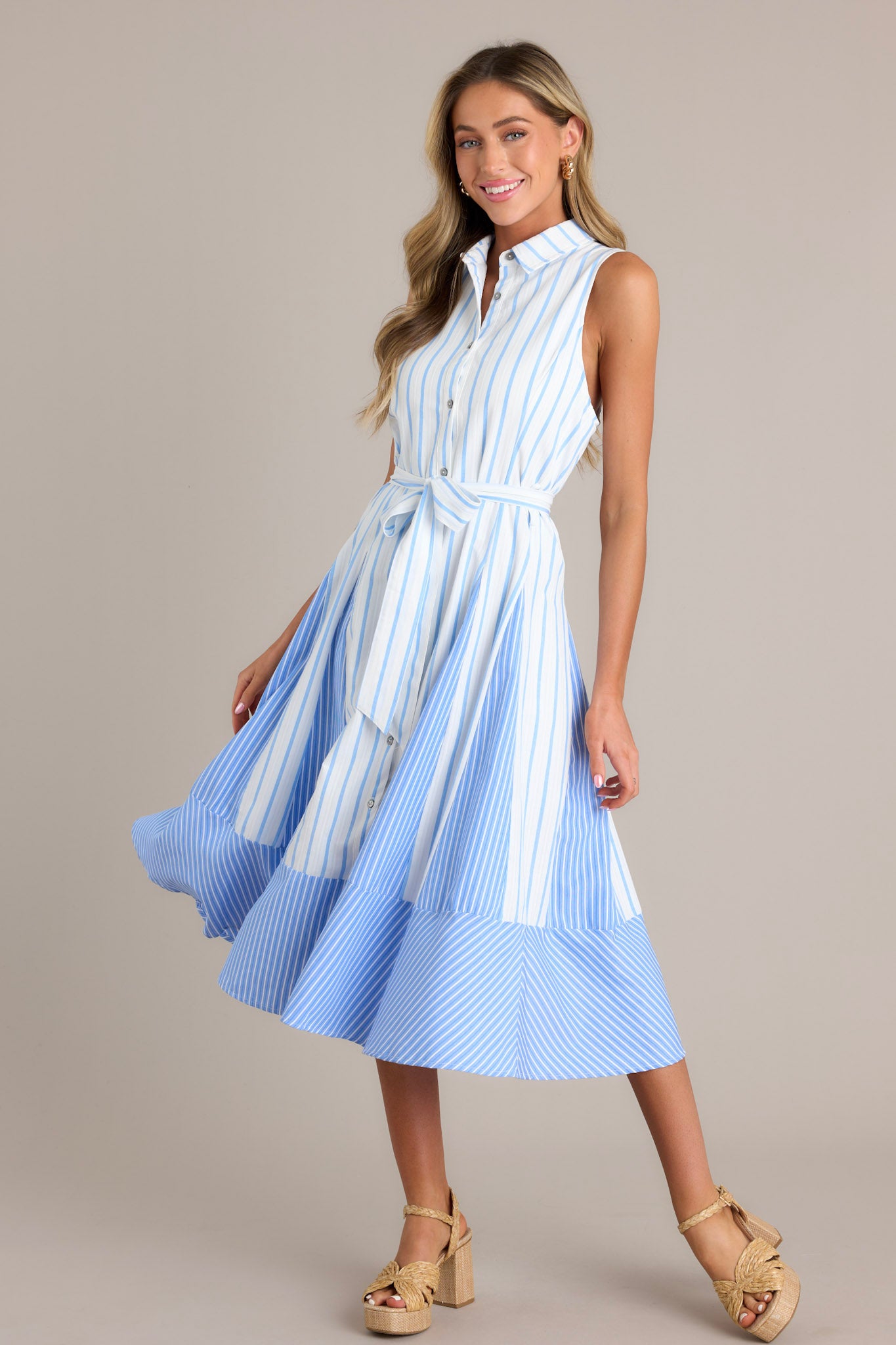 Action shot of a light blue midi dress with a collared neckline, a functional button front, a self-tie waist belt, a unique stripe pattern, and a flowing silhouette, highlighting the dress's flow and movement.