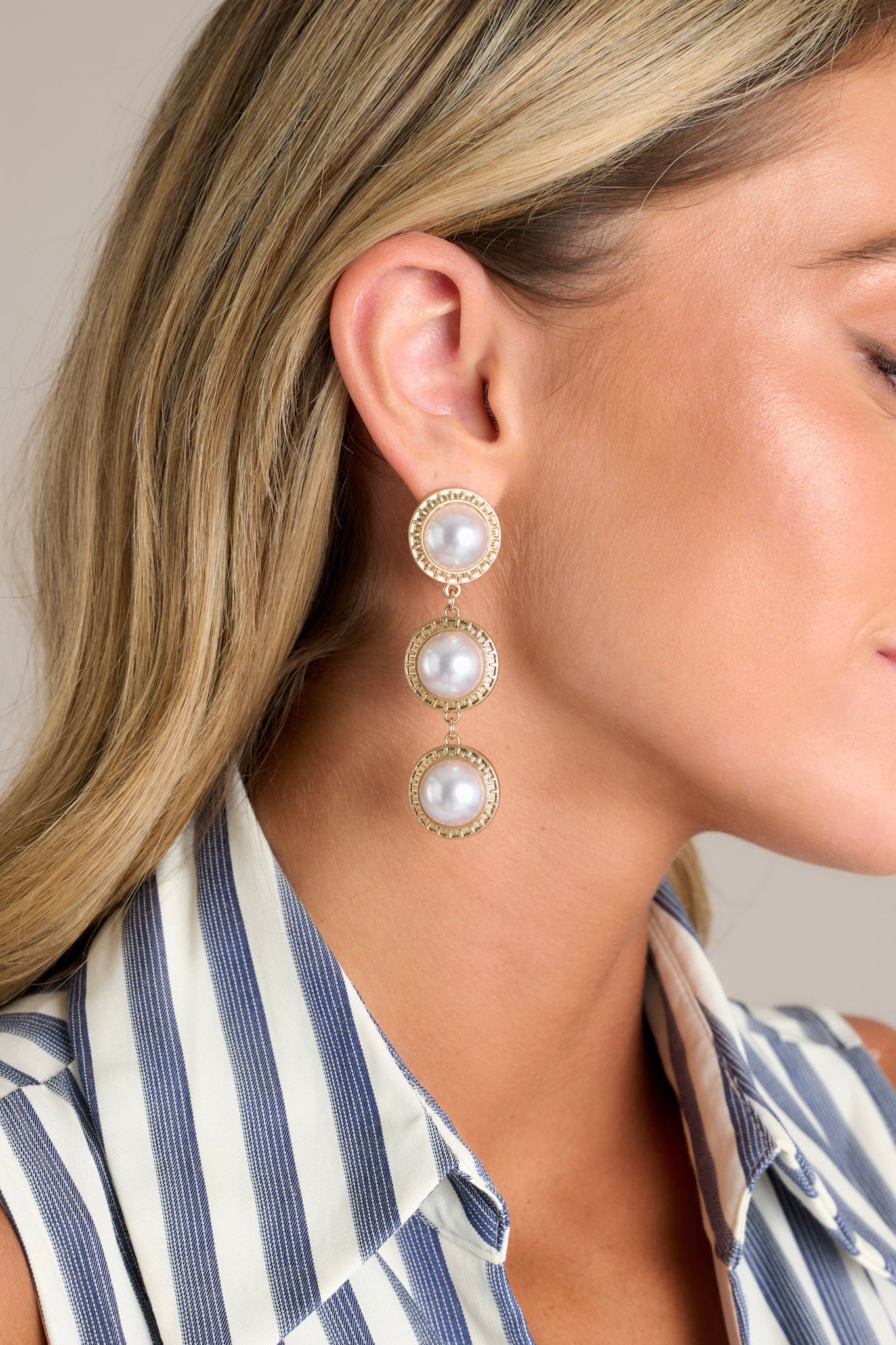 These gold pearl earrings feature three round hanging ivory faux pearls with textured gold borders, and secure post backings.