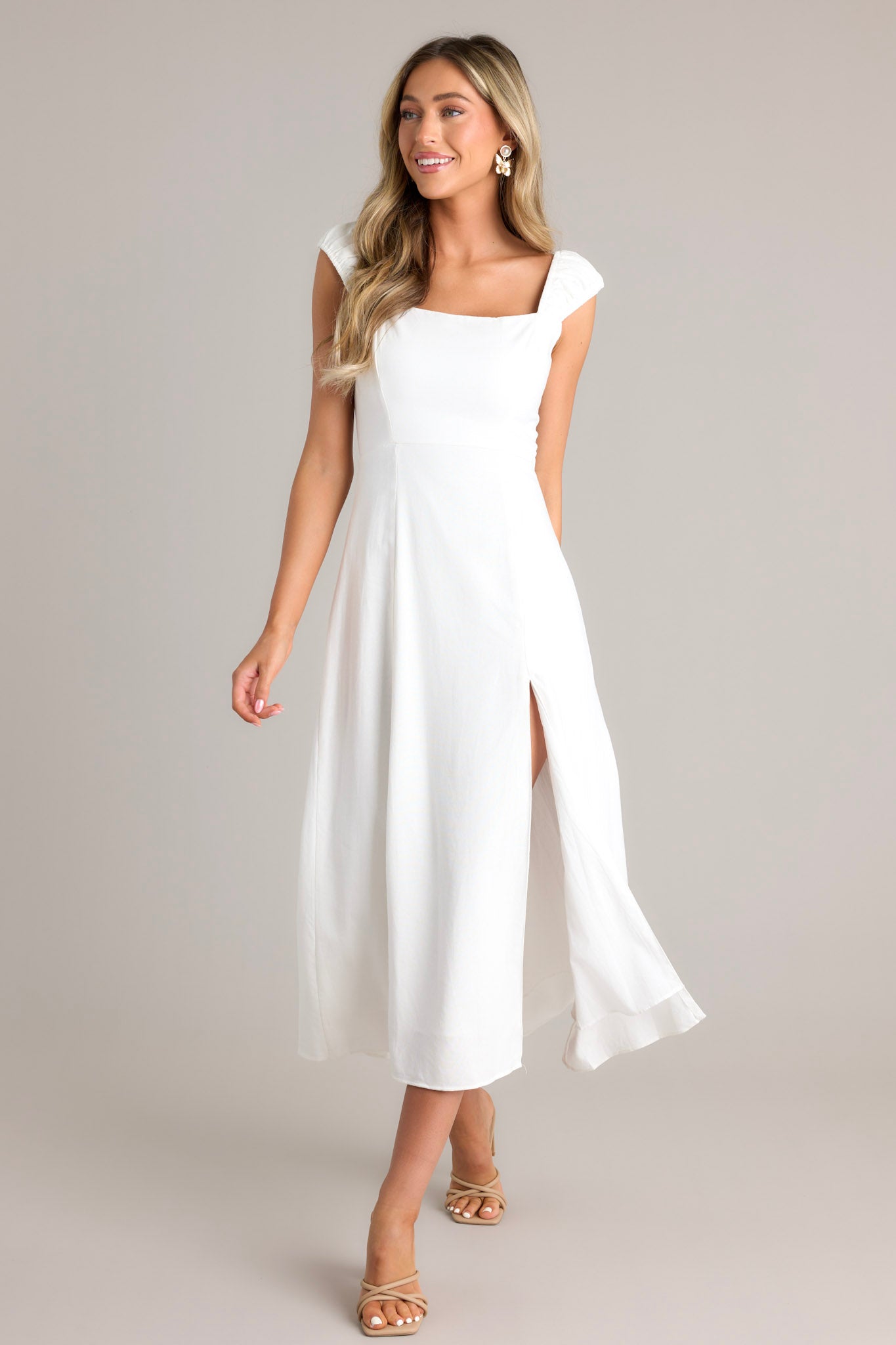 Action shot of a white midi dress with a square neckline, smocked back section, hidden zipper, smocked sleeves, leg slit, and flowy skirt, highlighting the movement.