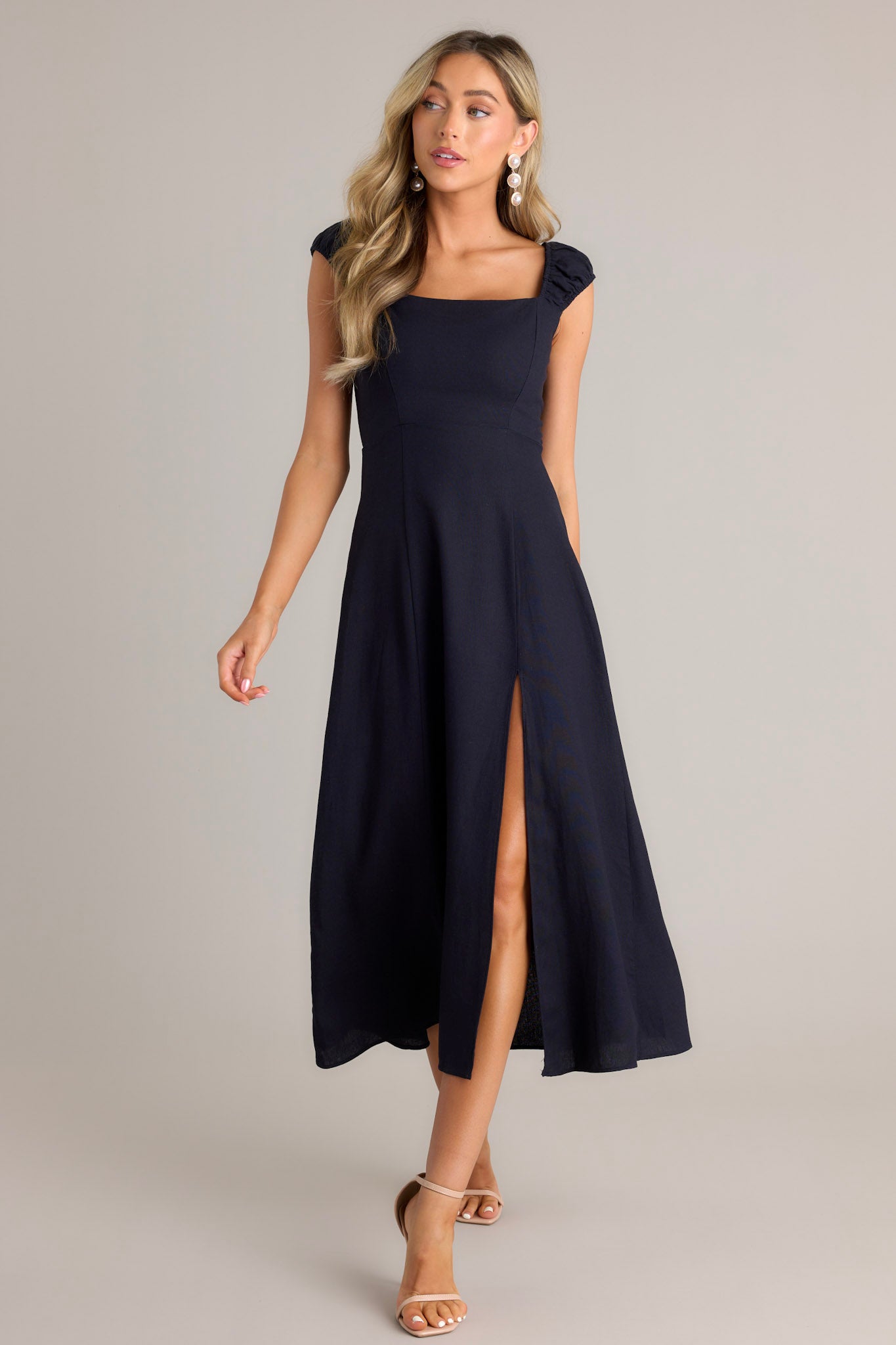 Action shot of a navy midi dress displaying the flow and movement of the skirt, highlighting the square neckline, smocked sleeves, and slit up the leg.