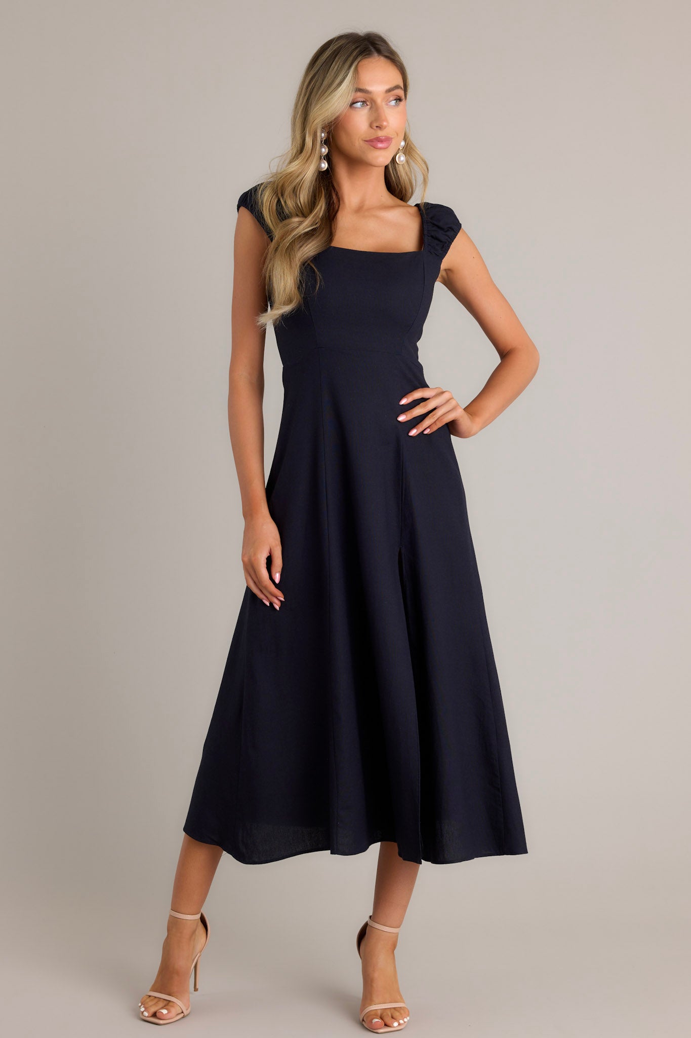 Front angled view of a navy midi dress featuring a square neckline, smocked sleeves, slit up the leg, and a flowy skirt